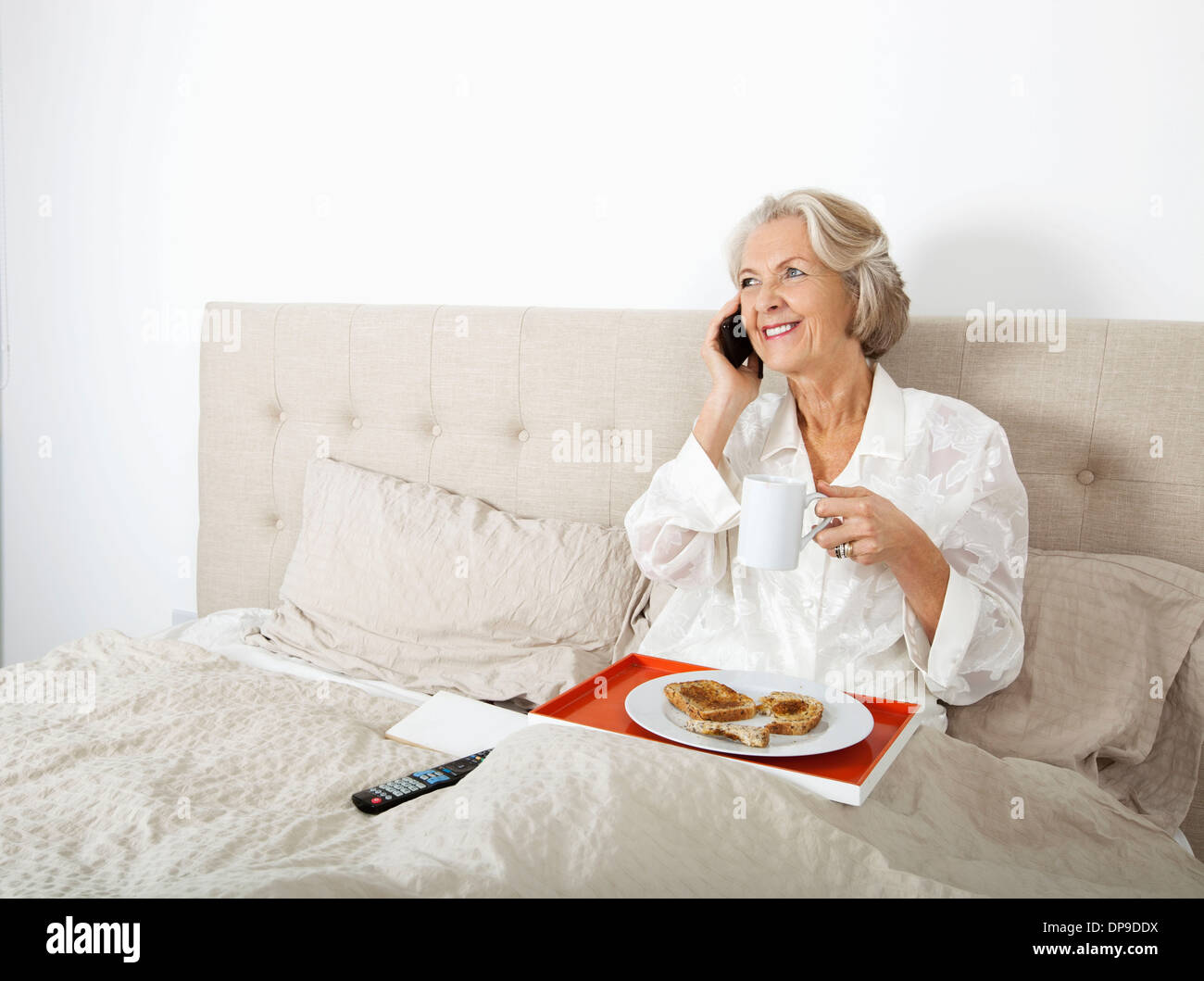 Beautiful senior Woman Beantwortung Handy beim Frühstück im Bett Stockfoto