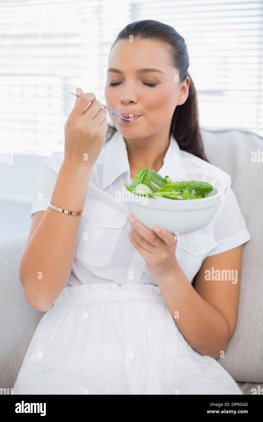 Entspannte hübsche Frau essen gesunde Salat auf sofa Stockfoto