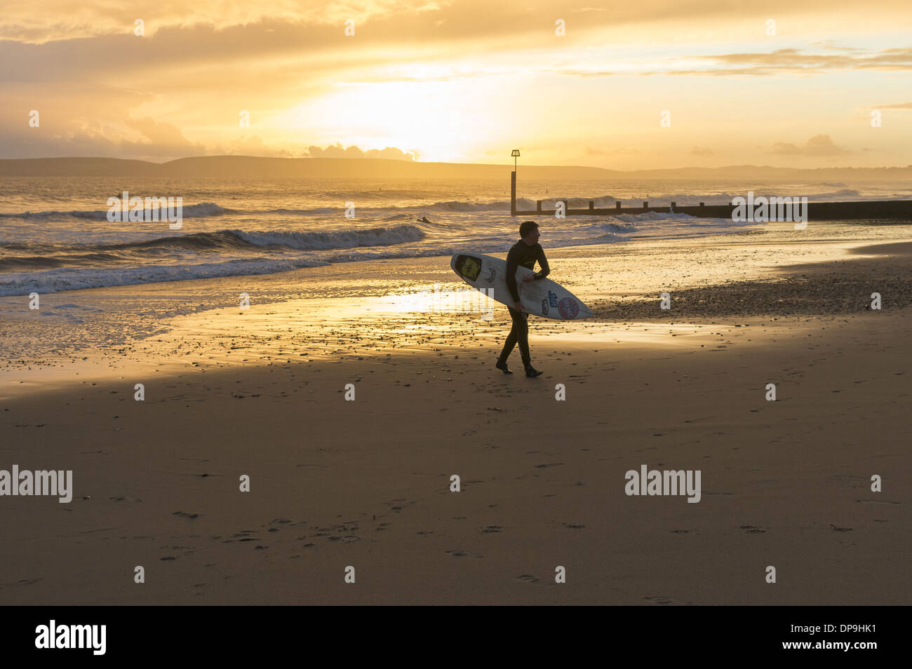 Surfer, die den Strand mit herrlichem Sonnenuntergang in Boscombe, Bournemouth, Dorset, England, Großbritannien, hinauflaufen Stockfoto