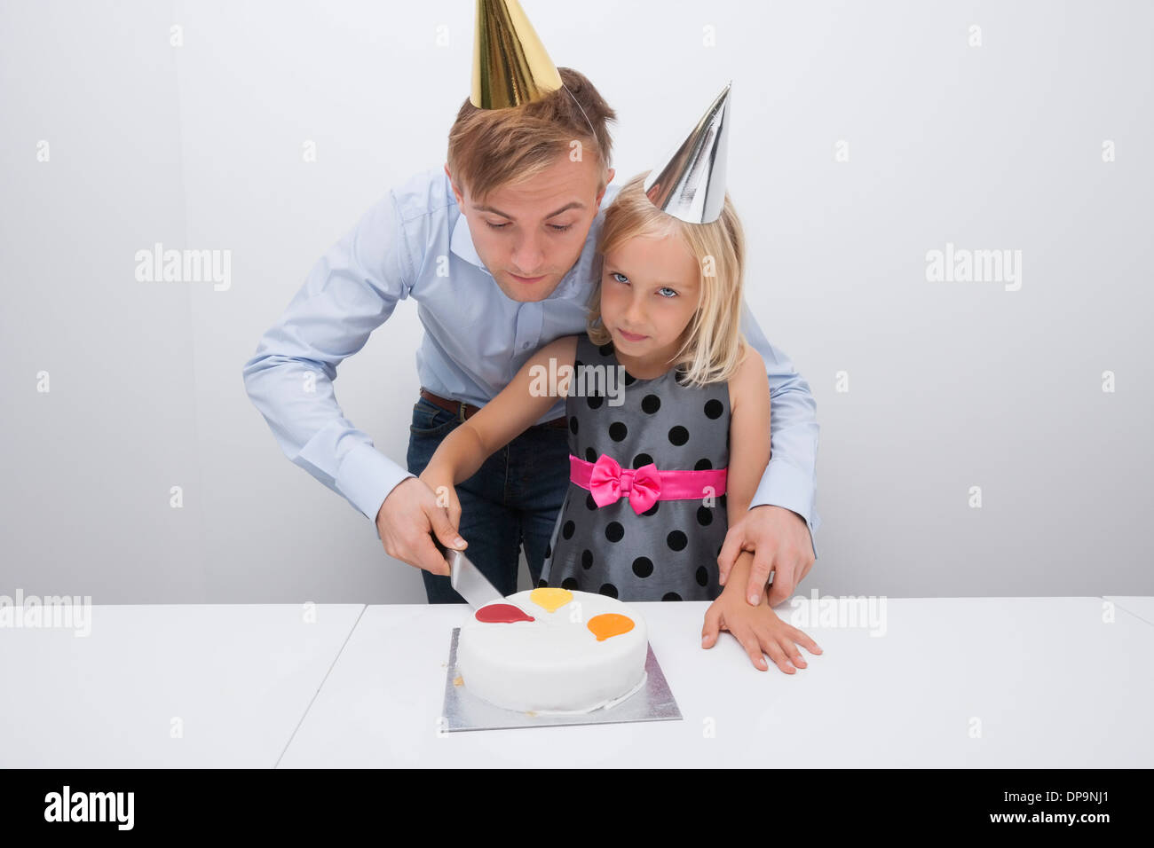 Vater und Tochter schneiden Geburtstagskuchen am Tisch Stockfoto