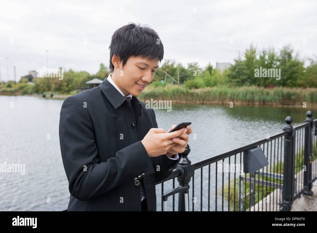 Glücklich Mitte adult Geschäftsmann von SMS-Nachrichten über Mobiltelefon am Brückengeländer Stockfoto