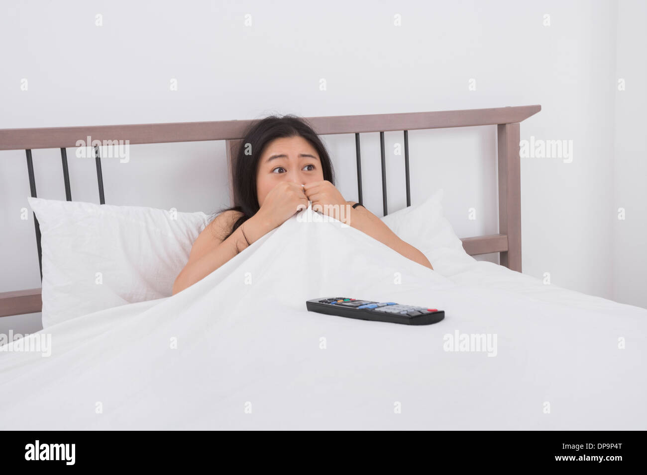 Verängstigte Frau Fernsehen im Bett Stockfoto