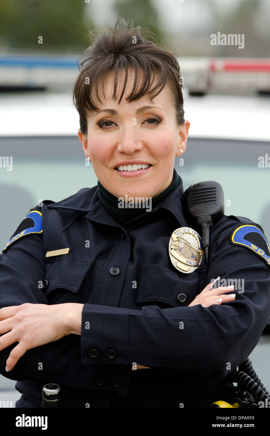 eine freundlich und lächelnd Hispanic Polizistin mit ihrem Streifenwagen. Stockfoto