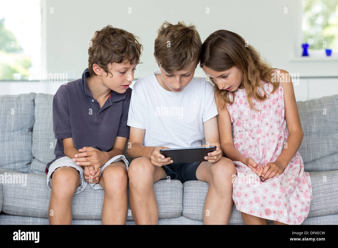 Brüder und Schwester auf Sofa Blick auf digital-Tablette Stockfoto