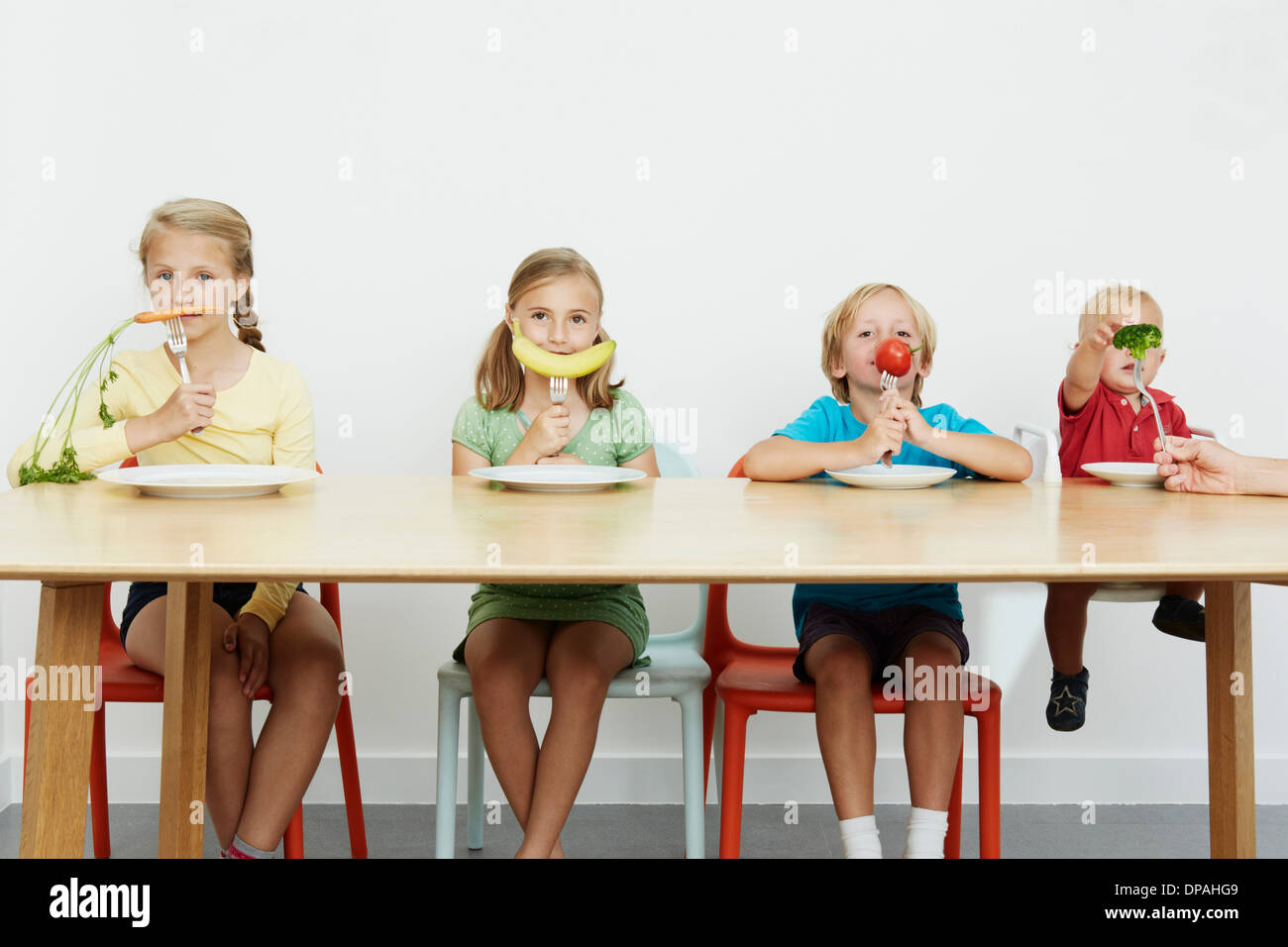 Vier Kinder sitzen am Tisch mit Gemüse auf Gabeln Stockfoto