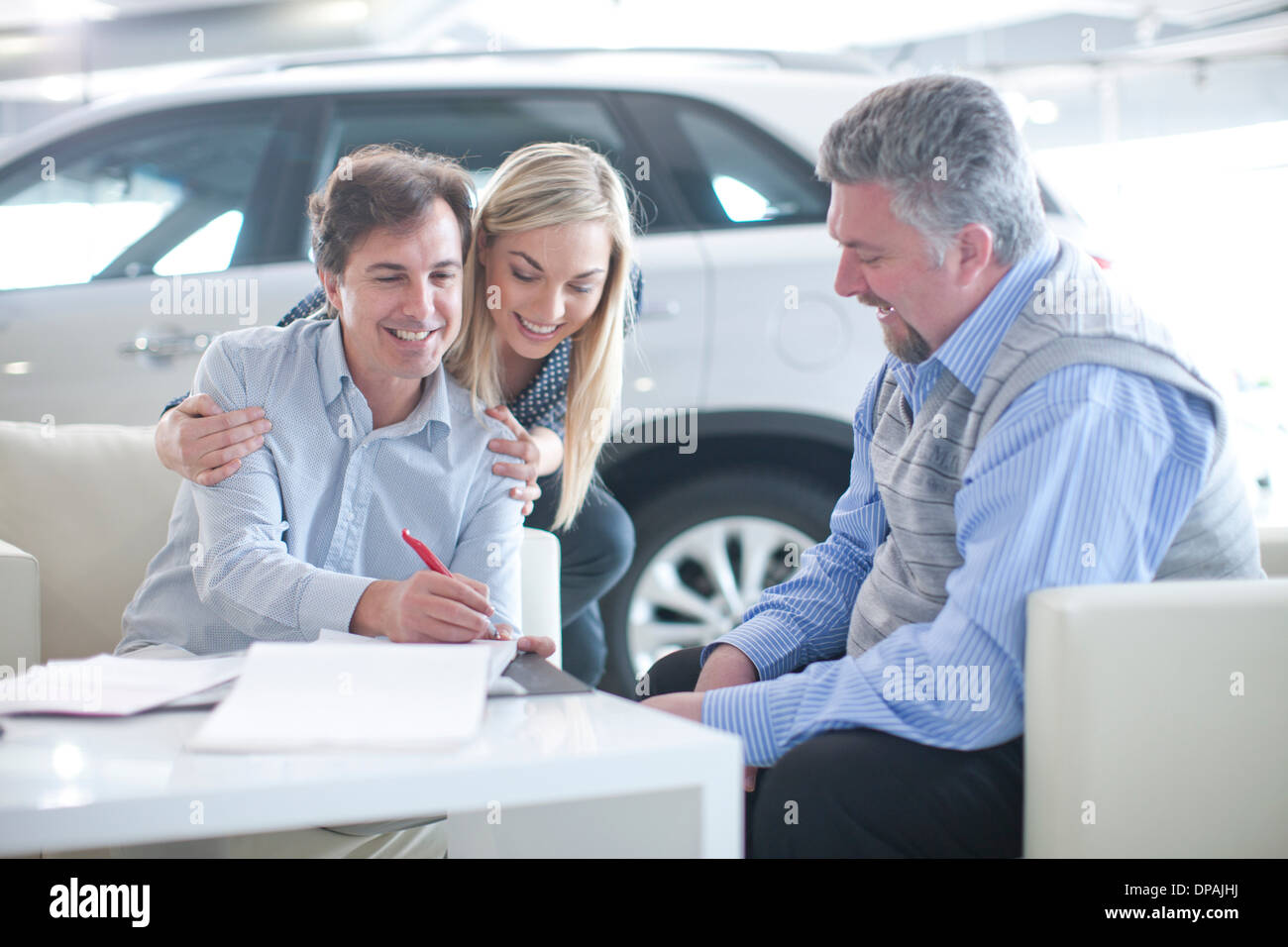 Autoverkäufer und paar Unterzeichnung Arbeitsvertrag in Autohaus Stockfoto