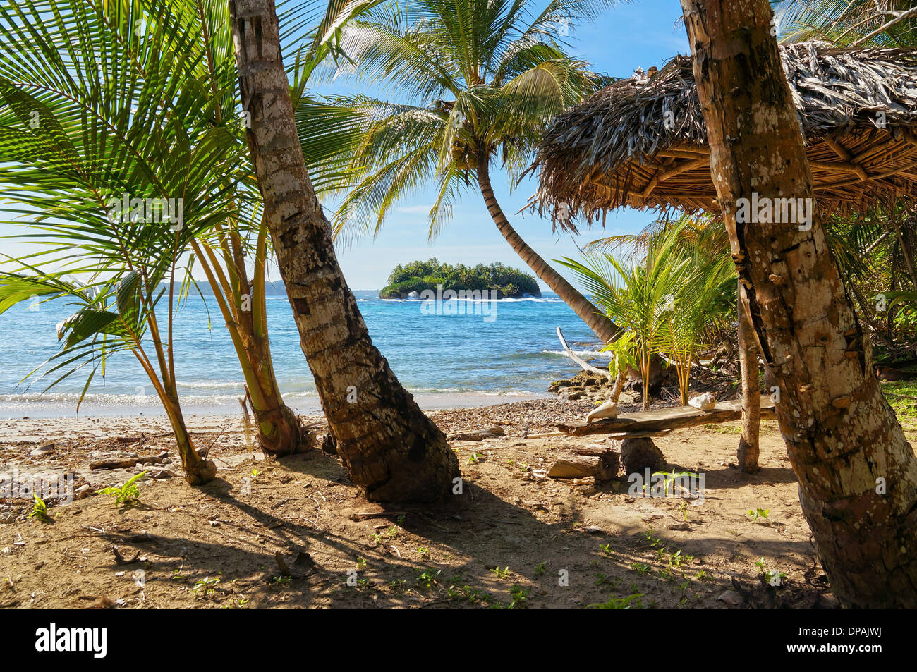 Tropischer Strand mit einem strohgedeckten Dach unter Kokospalmen und eine Insel am Horizont, Karibik, Bastimentos, Panama Stockfoto