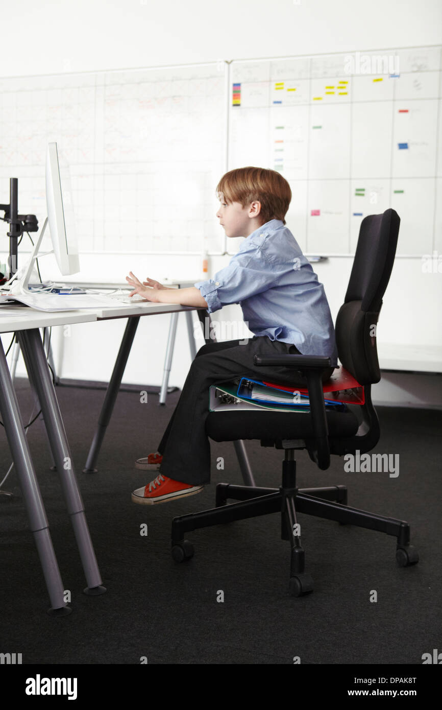 Junge sitzt auf Ringbücher auf Bürostuhl mit computer Stockfoto