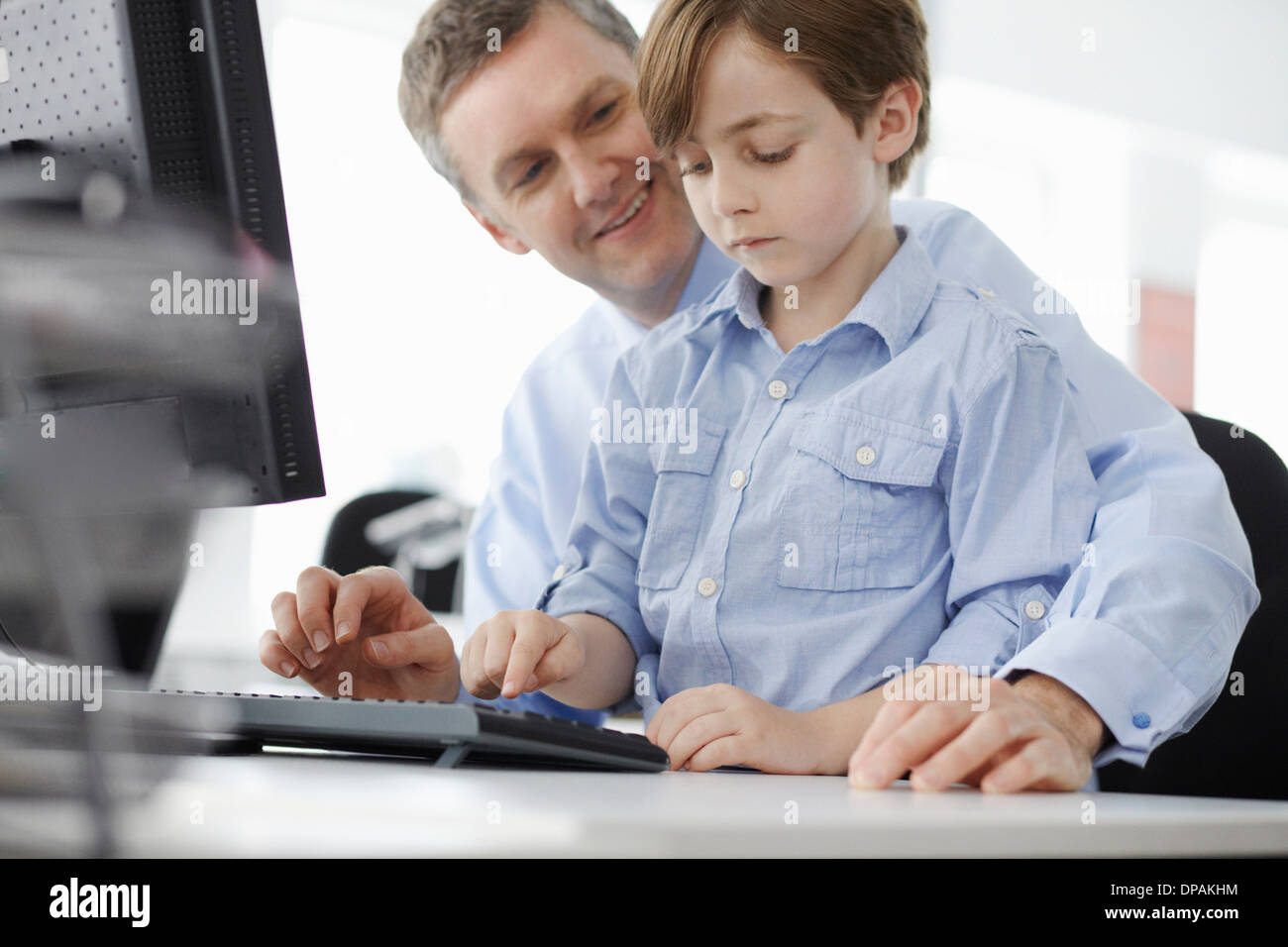 Junge sitzt auf Vaters Schoß mit Computer-Tastatur Stockfoto