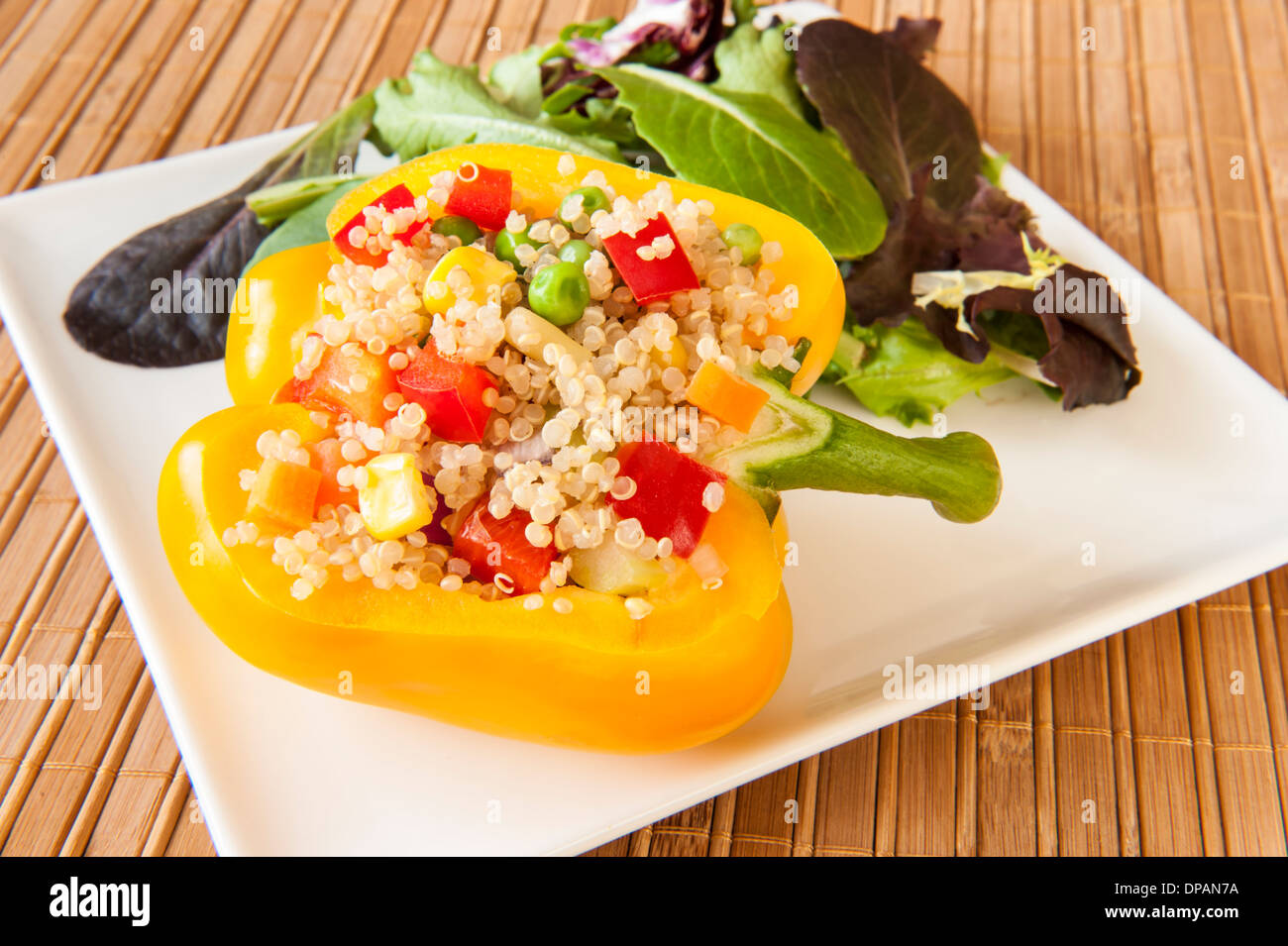 Gelbe Paprika gefüllt mit Quinoa und Gemüse auf einem weißen Teller mit gemischtem grünen Salat Stockfoto