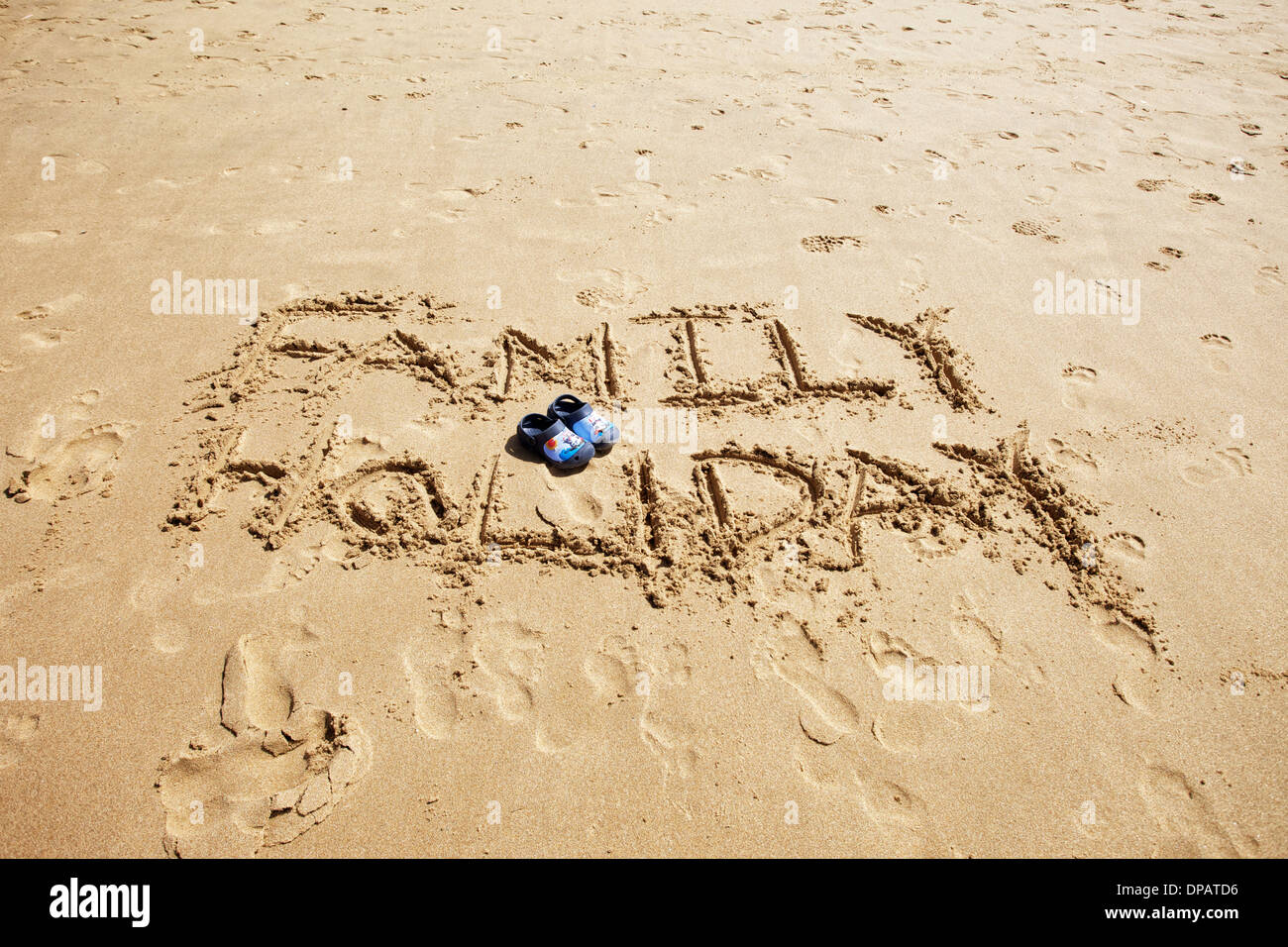 Nachrichten und Wörter in den Sand geschrieben am Strand mit Kids Crocs in Rosa und Blau im Bild. Aktuell für Reisebüros und Ferien Stockfoto