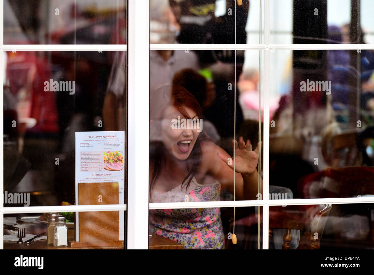 Hübsche junge Frau saß in einem Restaurant bei einem Freund gesehen durch das Fenster winken Stockfoto