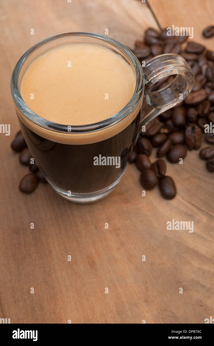 Glastasse Espresso auf Holztisch mit Kaffeebohnen mit Exemplar - geringe Schärfentiefe Stockfoto