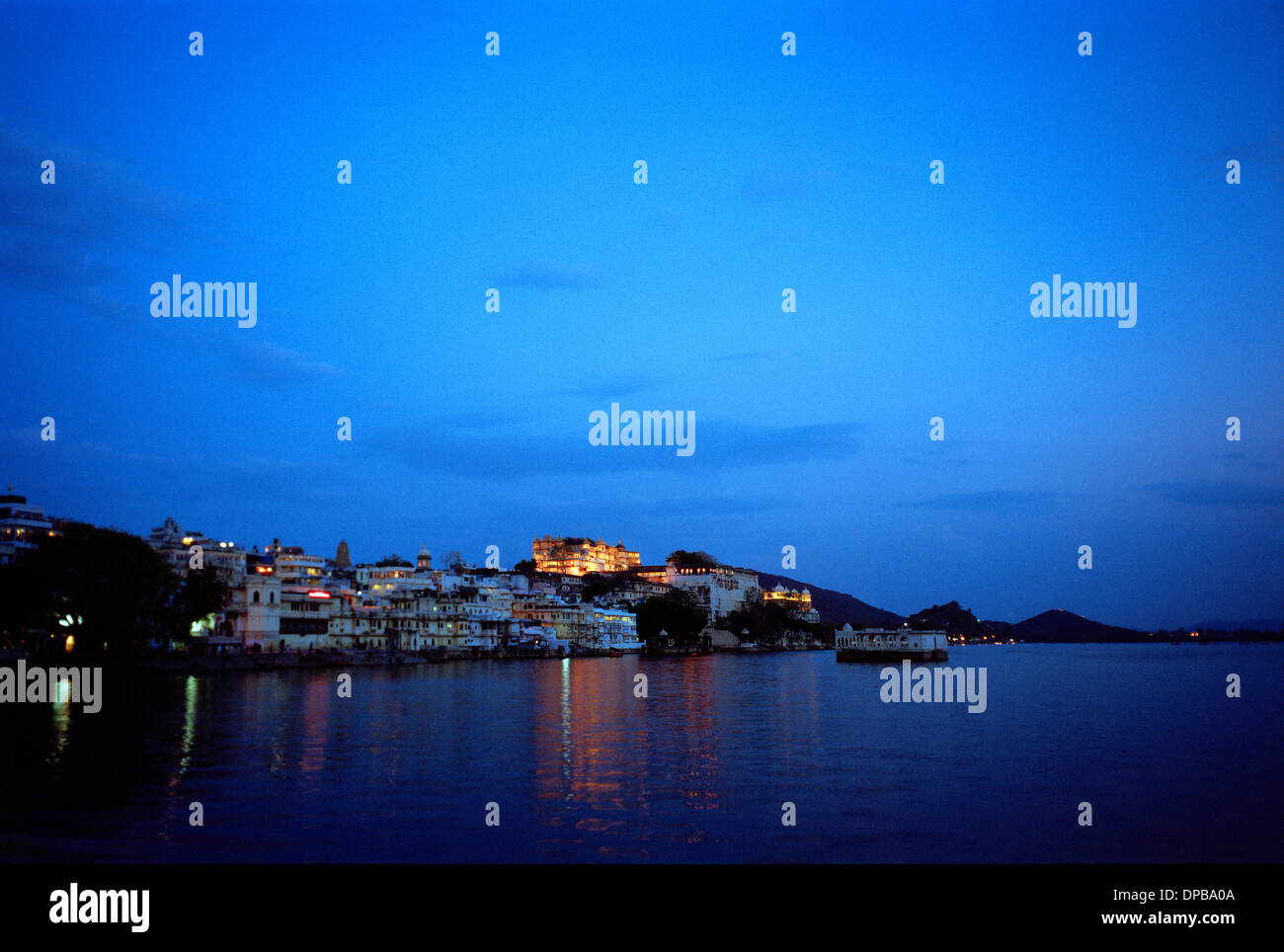 Ein Blick über Pichola-See, der City Palace in Udaipur in Rajasthan in Indien in Südasien. Sunset Blue Sky Travel Dämmerung Abenddämmerung Fernweh Stockfoto