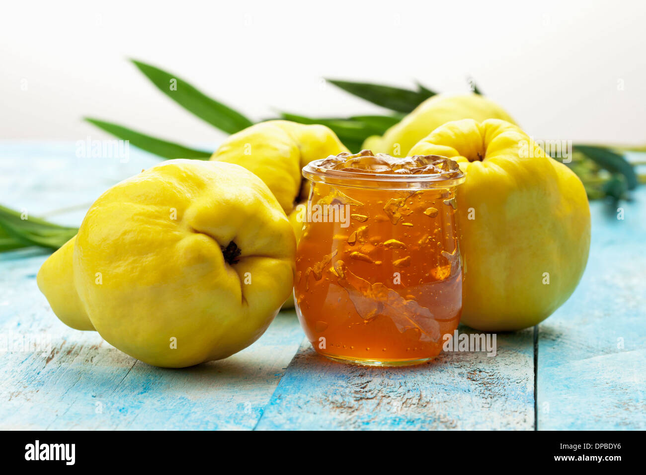 Vier Quitte (Cydonia Oblonga), ein Löffel und ein Glas von Quitten Marmelade auf Holztisch Stockfoto