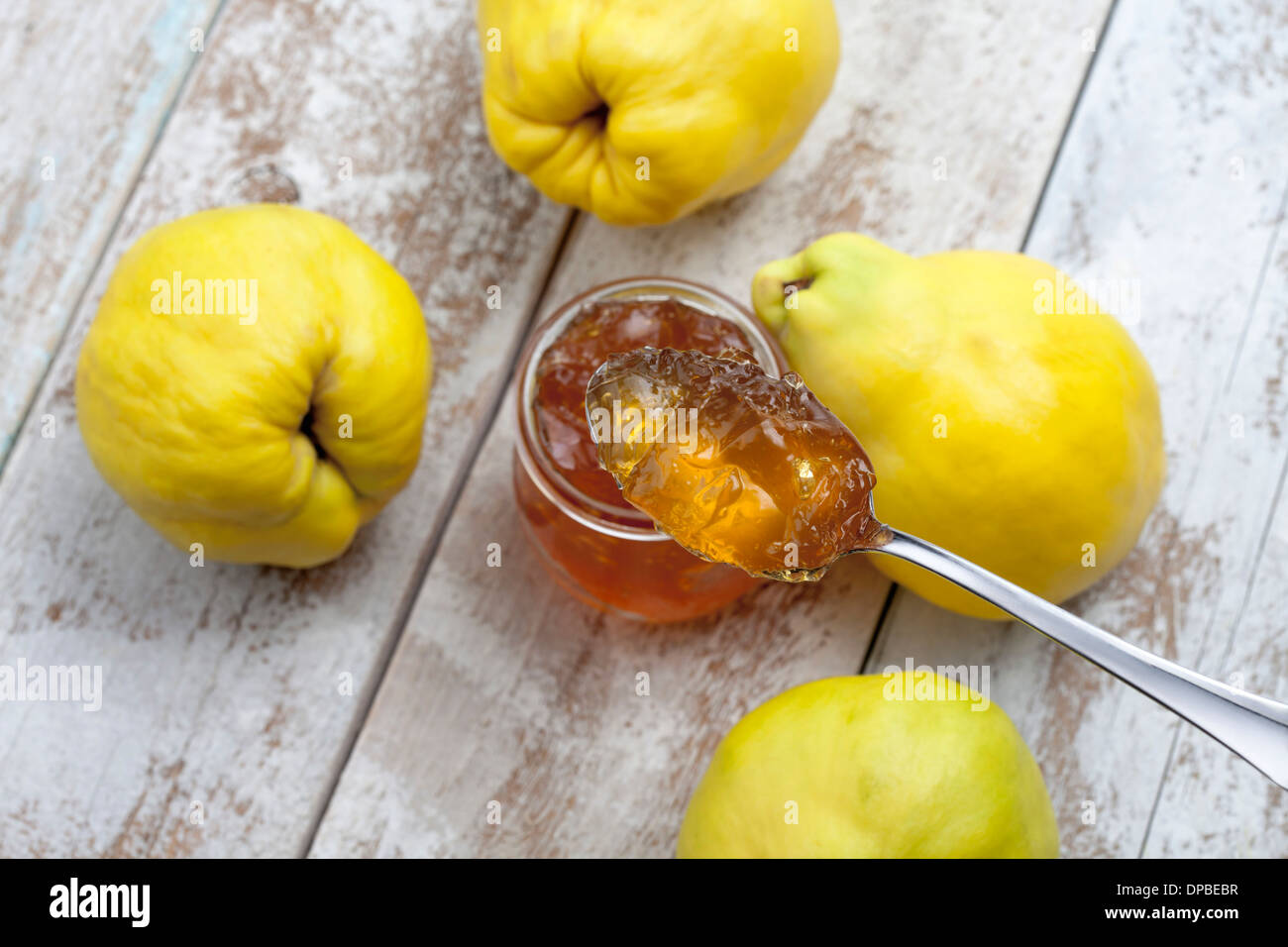 Vier Quitte (Cydonia Oblonga), ein Löffel und ein Glas von Quitten Marmelade auf Holztisch Stockfoto