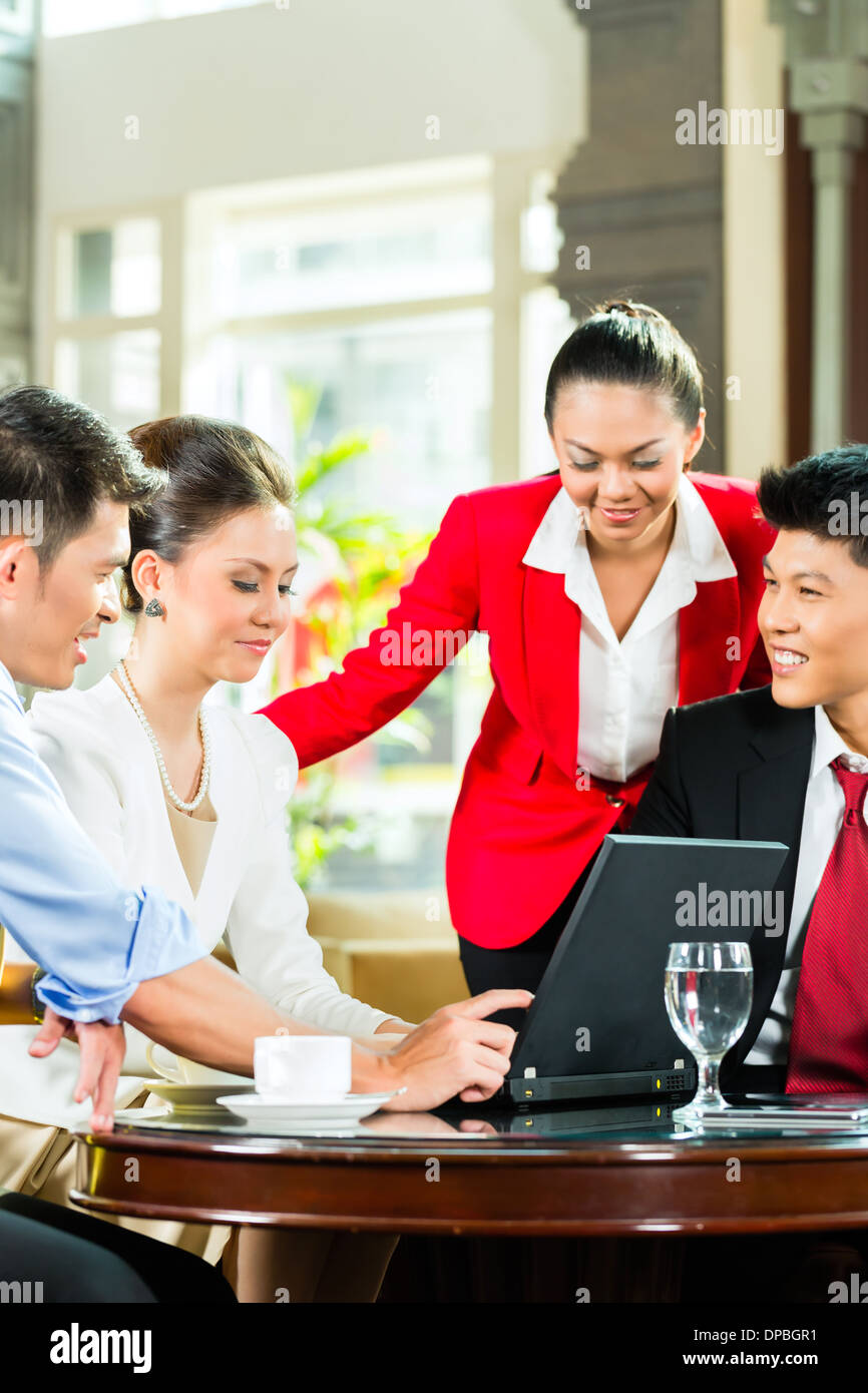 Vier asiatische chinesische Büro oder Unternehmer und Unternehmerinnen, die ein Geschäftstreffen in einer Hotellobby Dokument diskutieren Stockfoto