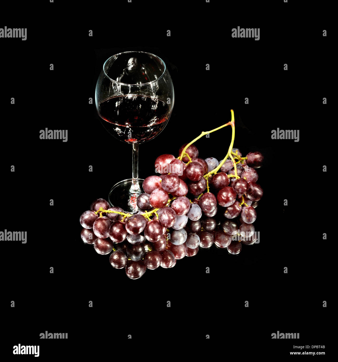 Trauben und ein Glas Rotwein auf einem schwarzen Hintergrund. Stockfoto