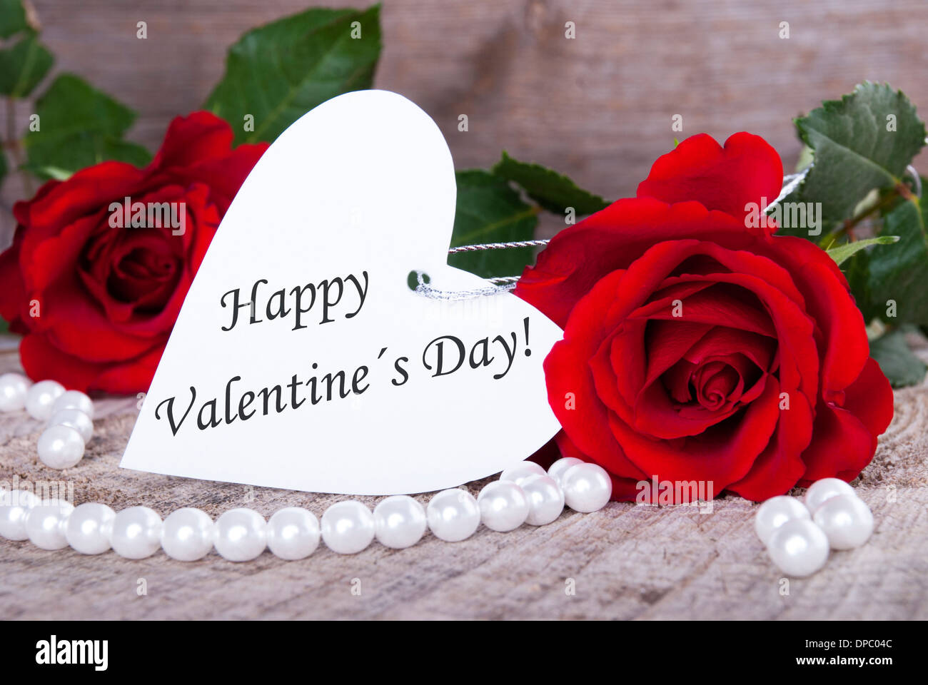 Ein weißes Herz mit Valentinstag Grüße drauf und rote Rosen Stockfoto