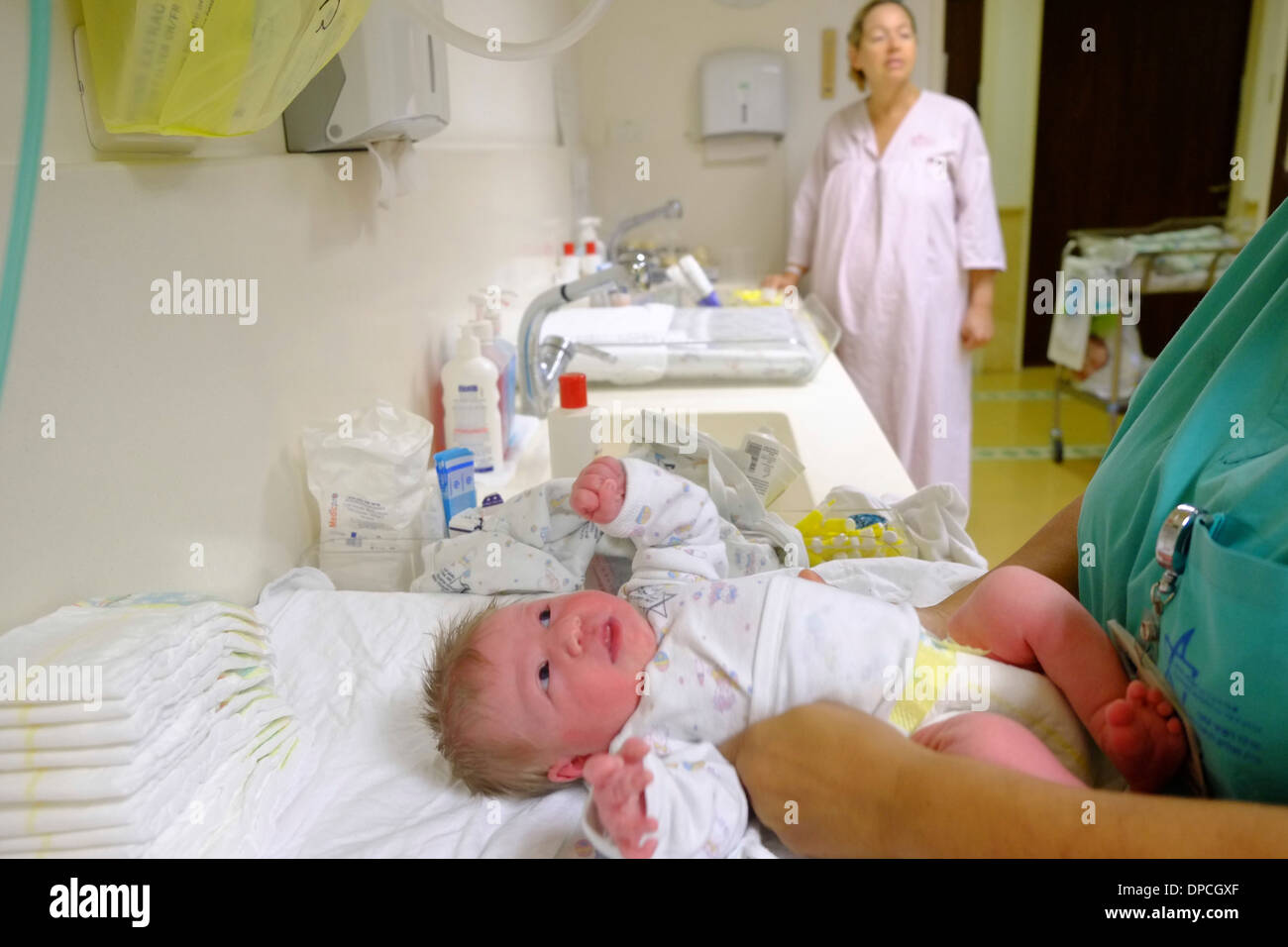 Krankenschwestern Kleider ein neugeborenes Kind in einer Entbindungsstation, während die Mutter Uhren Stockfoto