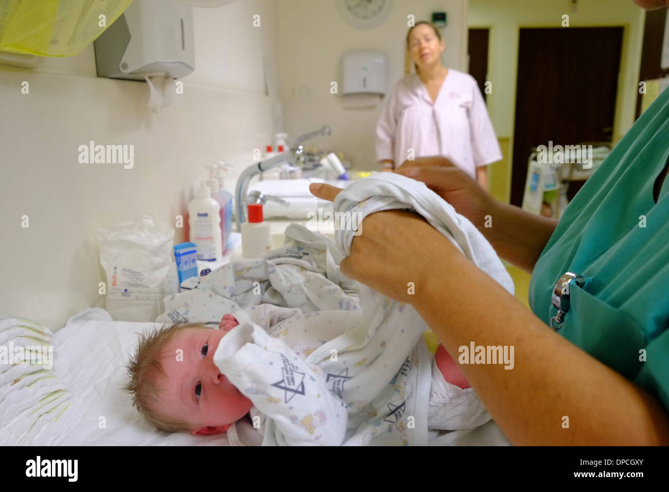 Krankenschwestern Kleider ein neugeborenes Kind in einer Entbindungsstation, während die Mutter Uhren Stockfoto