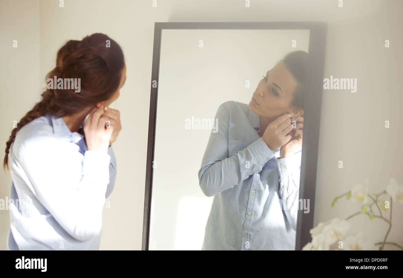 Schöne Frau ihren Ohrring vor Spiegel aufsetzen. Geschäftsfrau, die für die Arbeit anziehen. Kaukasische weibliches model Stockfoto
