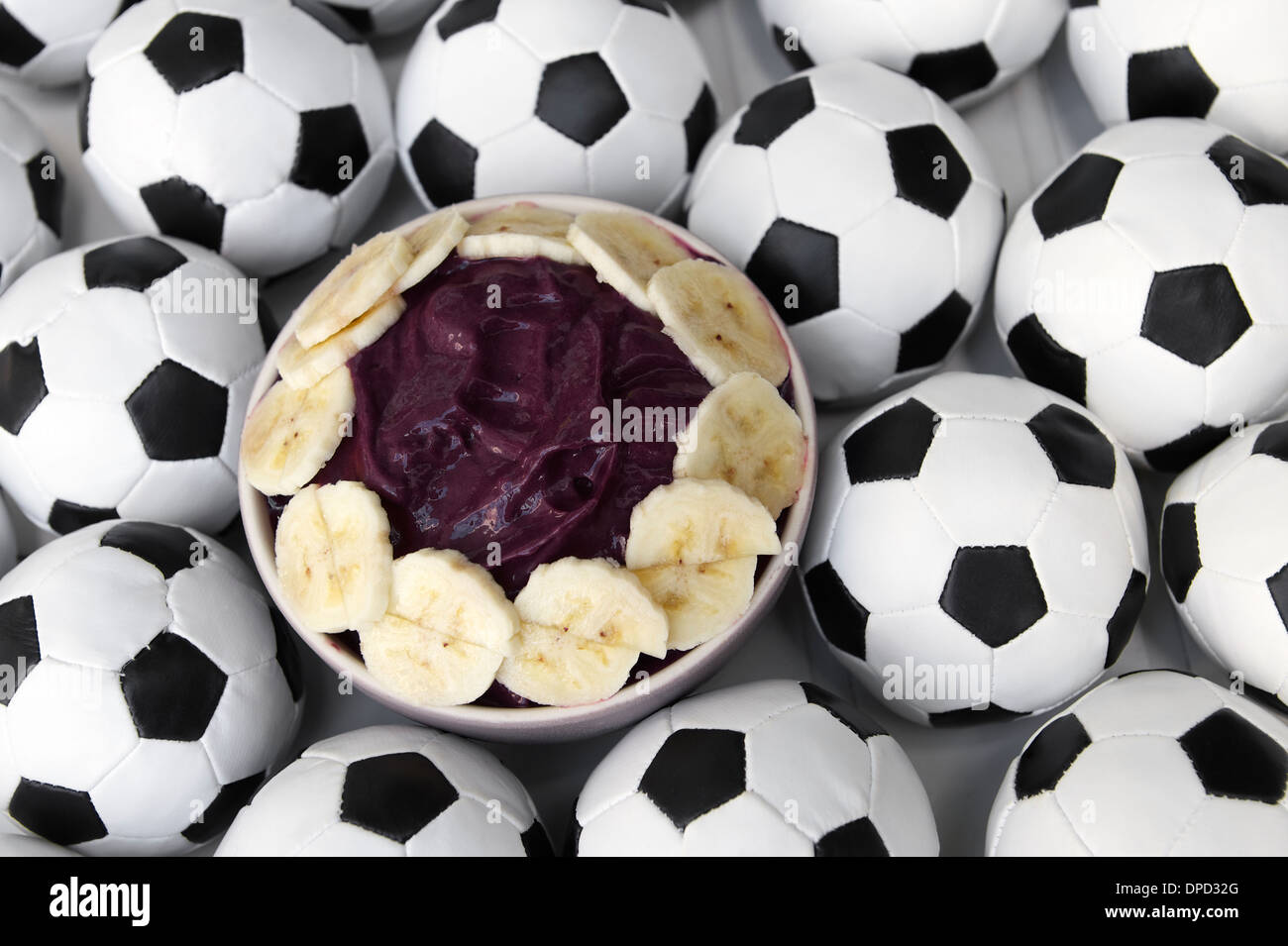 Brasilianischer Kultur auf dem Tisch verfügt über eine Schüssel mit frischen Acai mit Banane, umgeben von Fußball Fußbälle Stockfoto