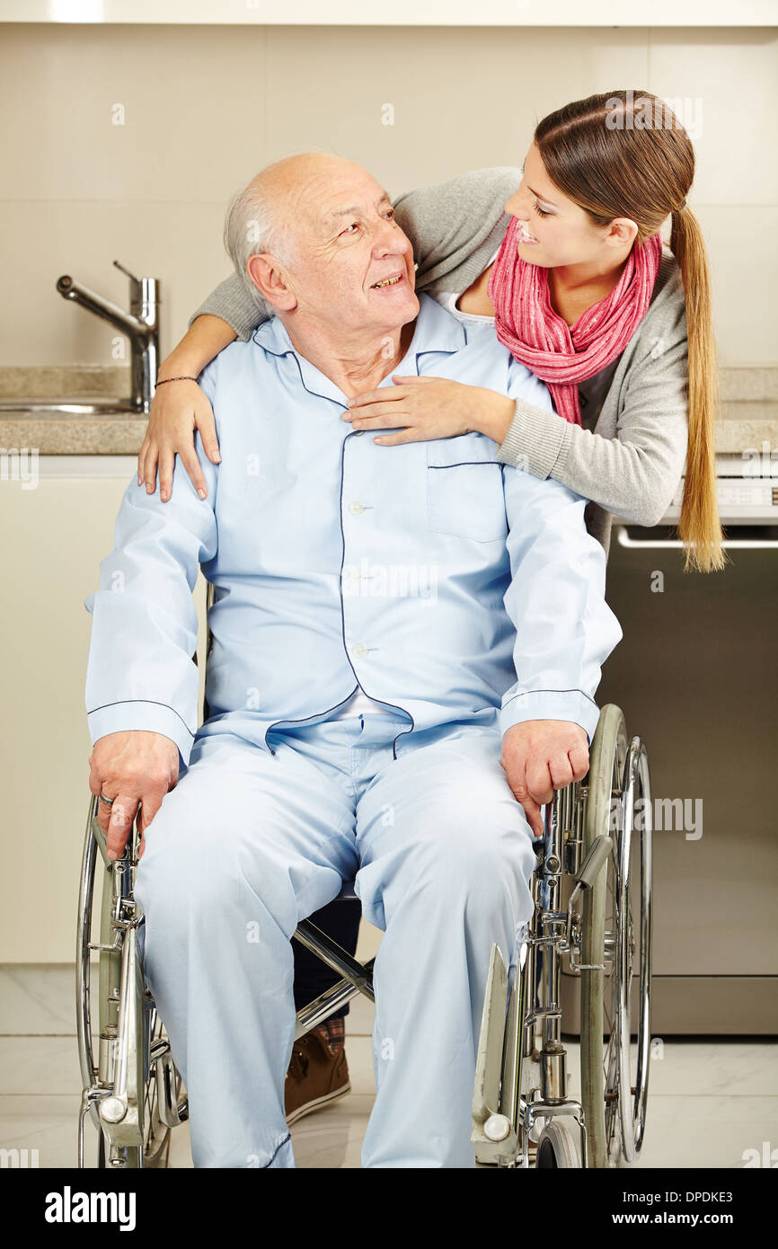 Glückliche junge Frau umarmt einen älteren Mann im Rollstuhl Stockfoto