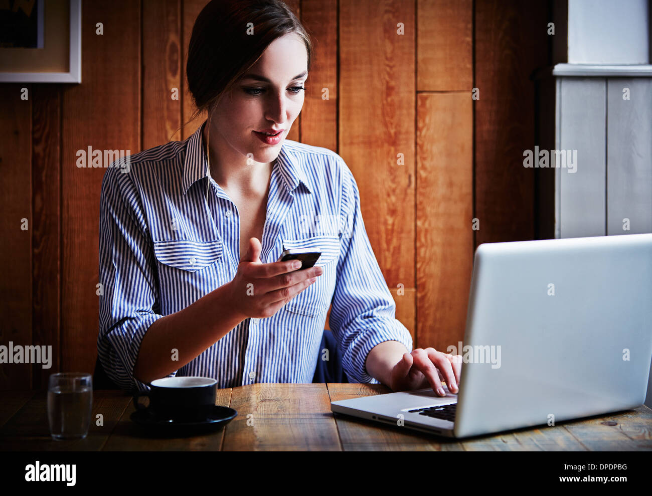 Junge Frau sitzt im Café halten Smartphone, Laptop-Computer mit Stockfoto