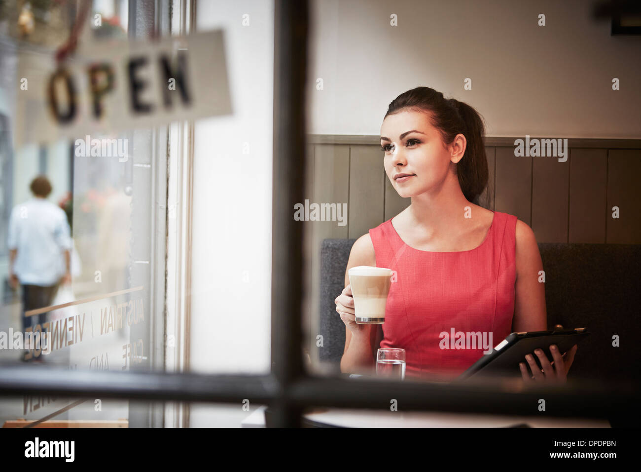 Junge Frau sitzt im Café mit digital-Tablette und Heißgetränk Stockfoto