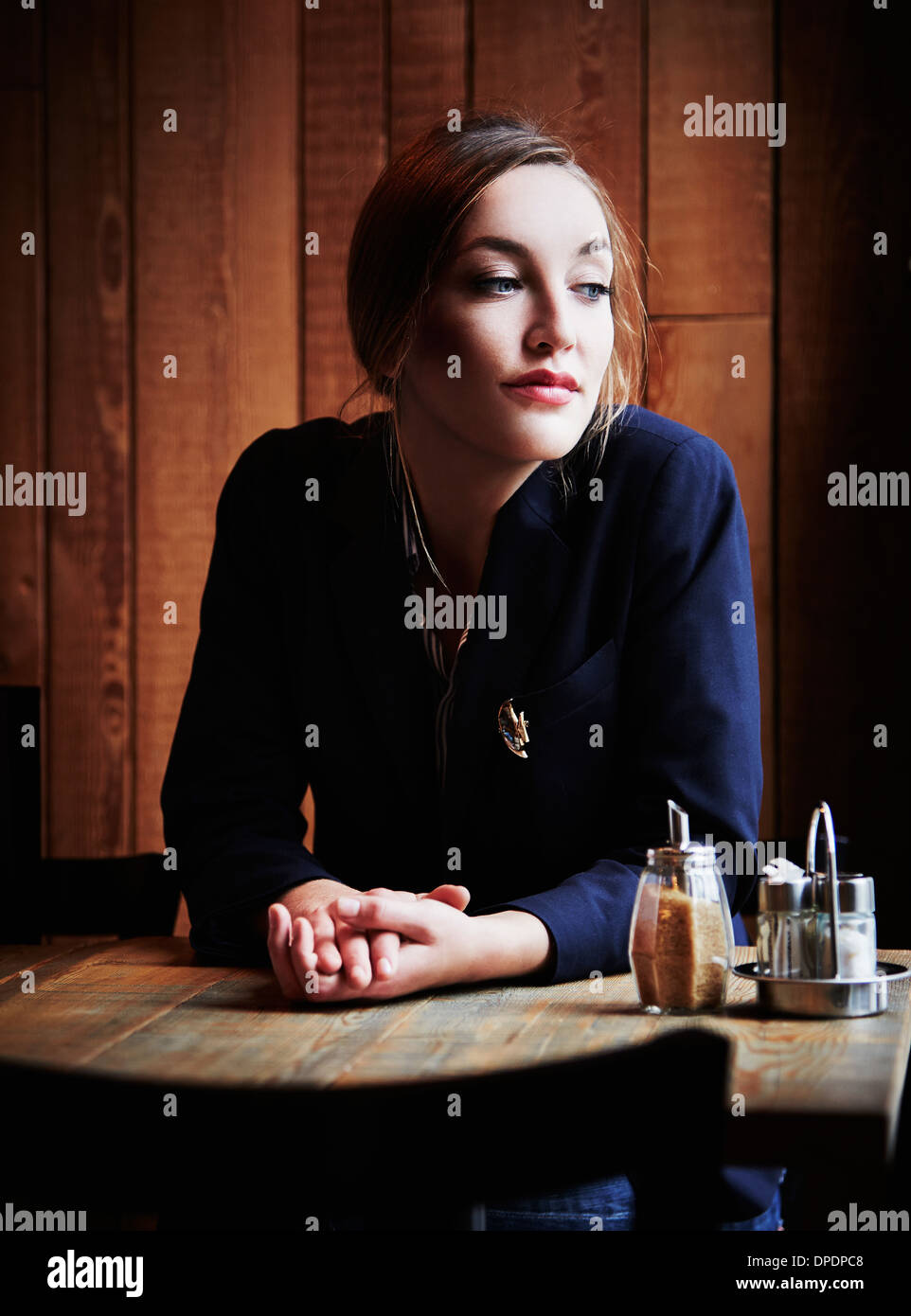 Junge Frau sitzt im Café mit den Händen umklammert Stockfoto