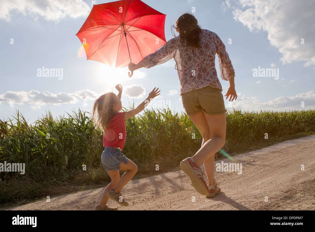 Mutter und Tochter ein Spaziergang durch Feld mit roten Regenschirm Stockfoto