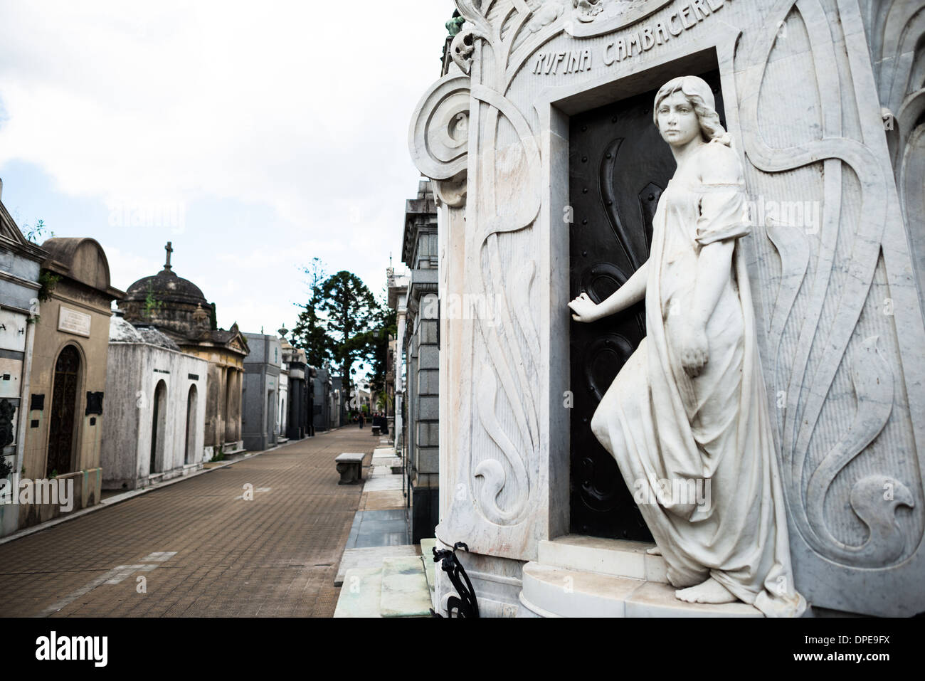 BUENOS AIRES, Argentinien – das Jugendstilmausoleum von Rufina Cambacérès auf dem Friedhof Recoleta (Cementerio de la Recoleta) zeigt eine lebensgroße Marmorstatue einer jungen Frau am Eingang. Das Grabmal erinnert an die tragische Geschichte der 19-jährigen Rufina, die angeblich erwacht ist, nachdem sie 1902 vorzeitig für tot erklärt worden war. Das skulpturale Detail der Figur, die die Grabtür zu öffnen scheint, spiegelt die eindringlichen Umstände ihres Todes wider. Stockfoto