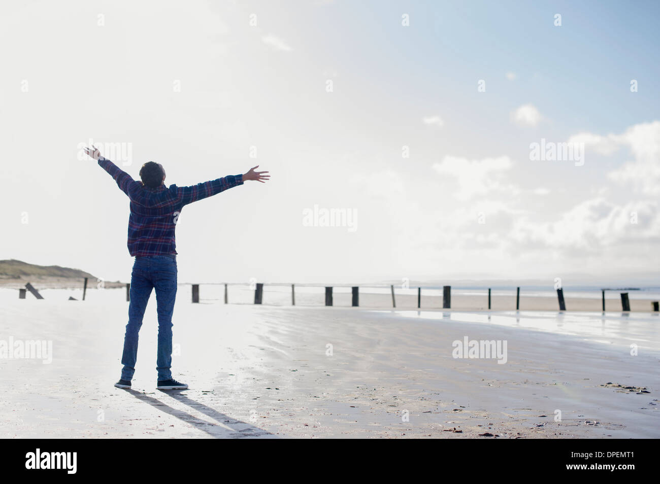 Junge Mann stand am Strand mit Armen, Brean Sands, Somerset, England Stockfoto