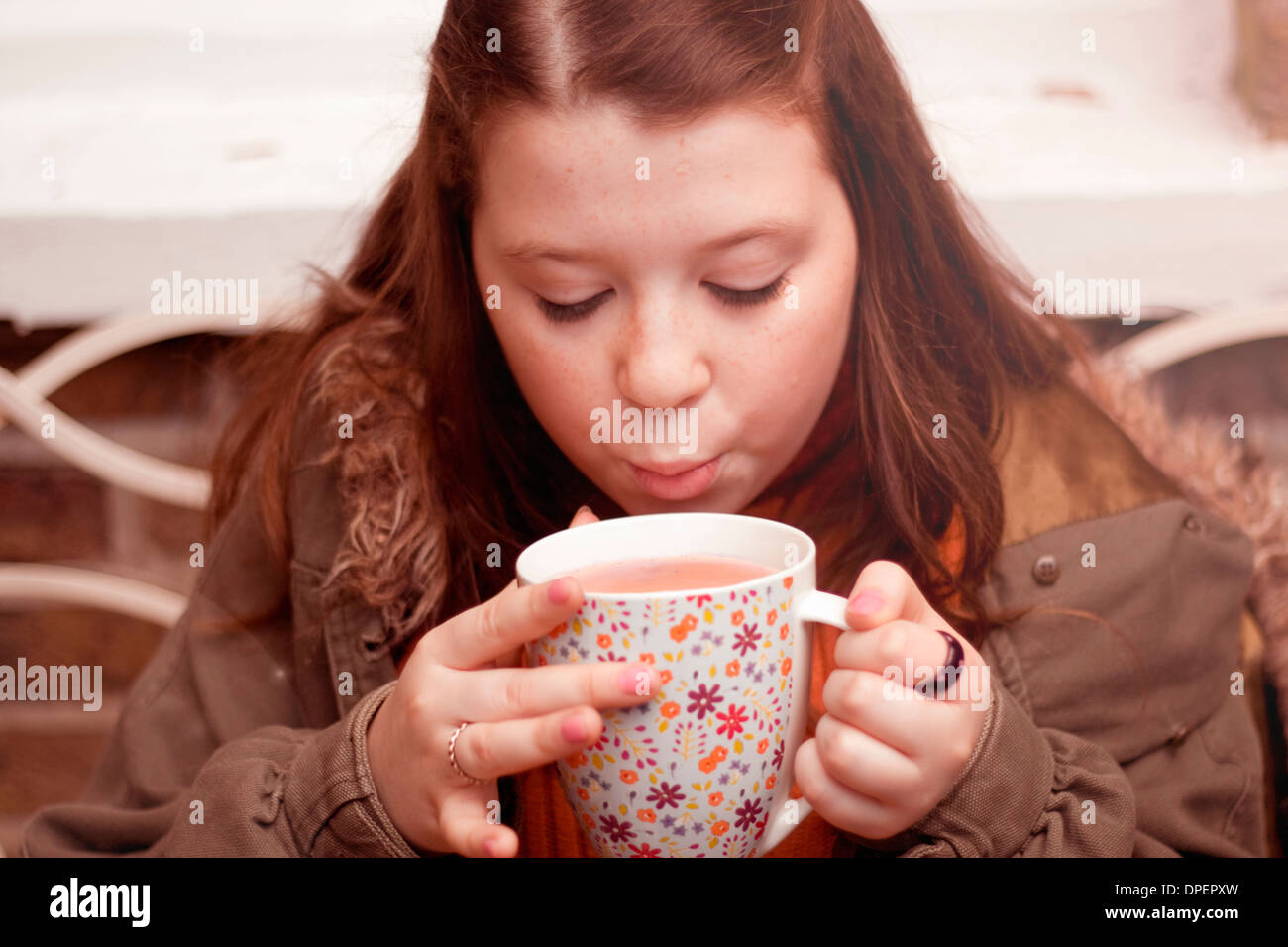 Junges Mädchen bläst auf Becher Kaffee im freien Stockfoto