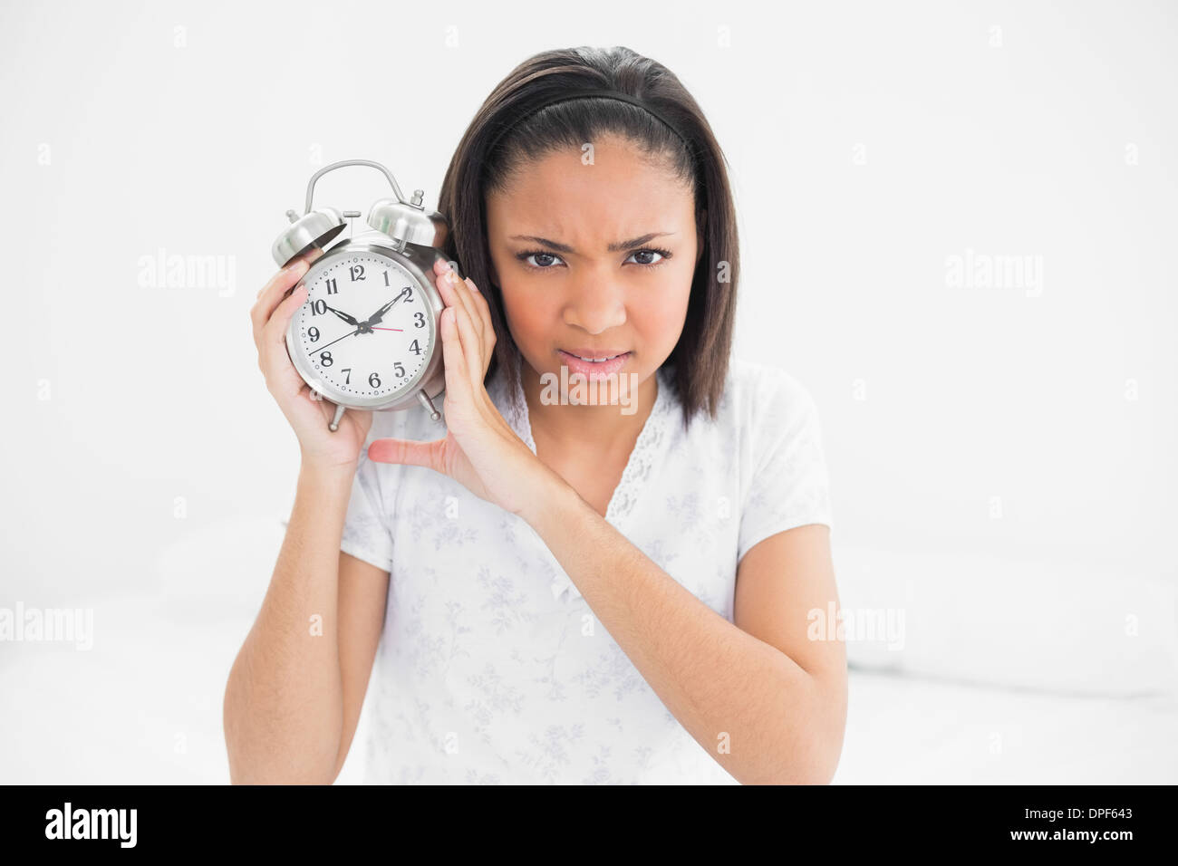 Stirnrunzelnd junge dunklen Haaren Modell hält einen Wecker Stockfoto