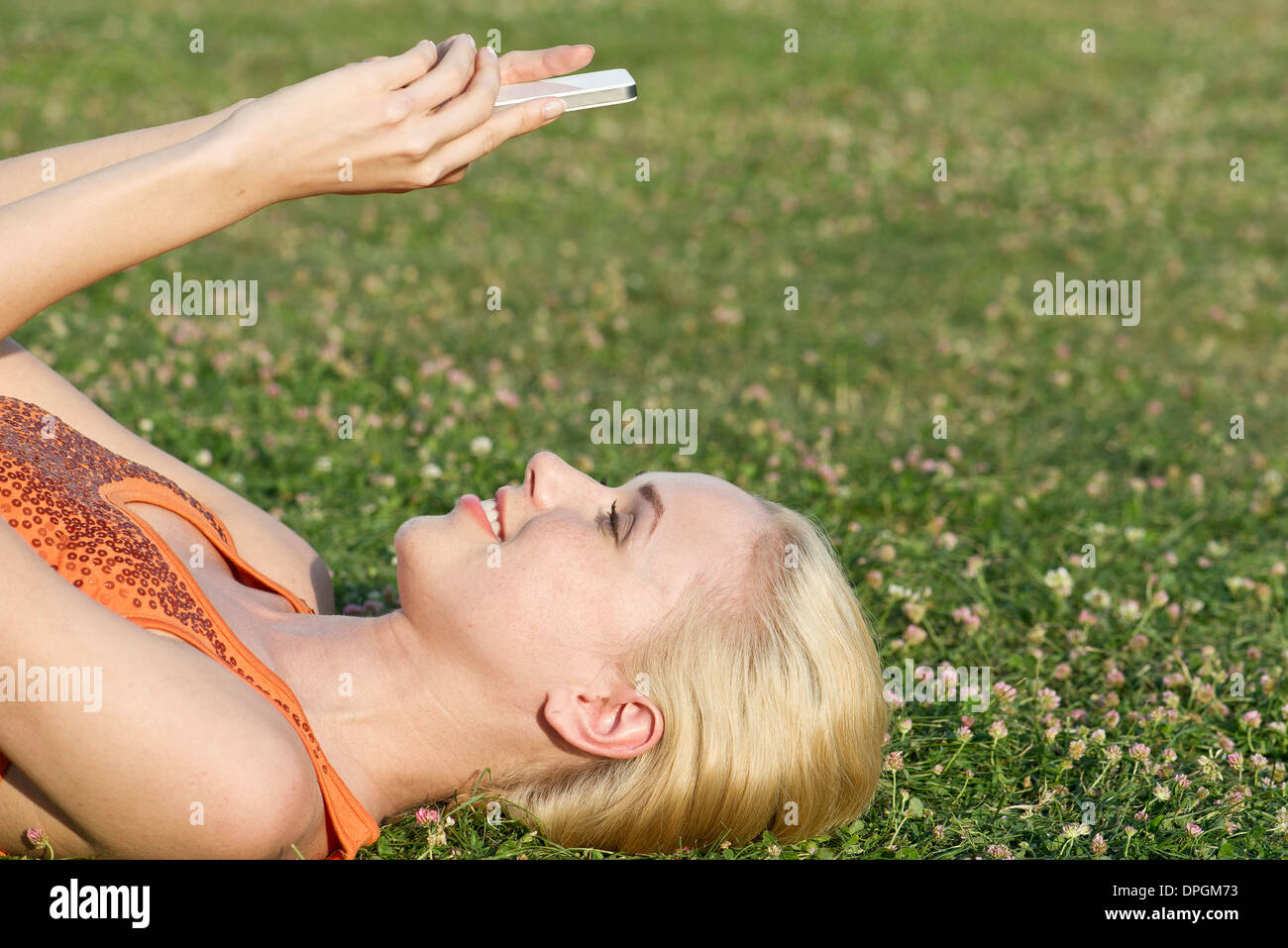Junge Frau liegt auf dem Rasen mit smartphone Stockfoto
