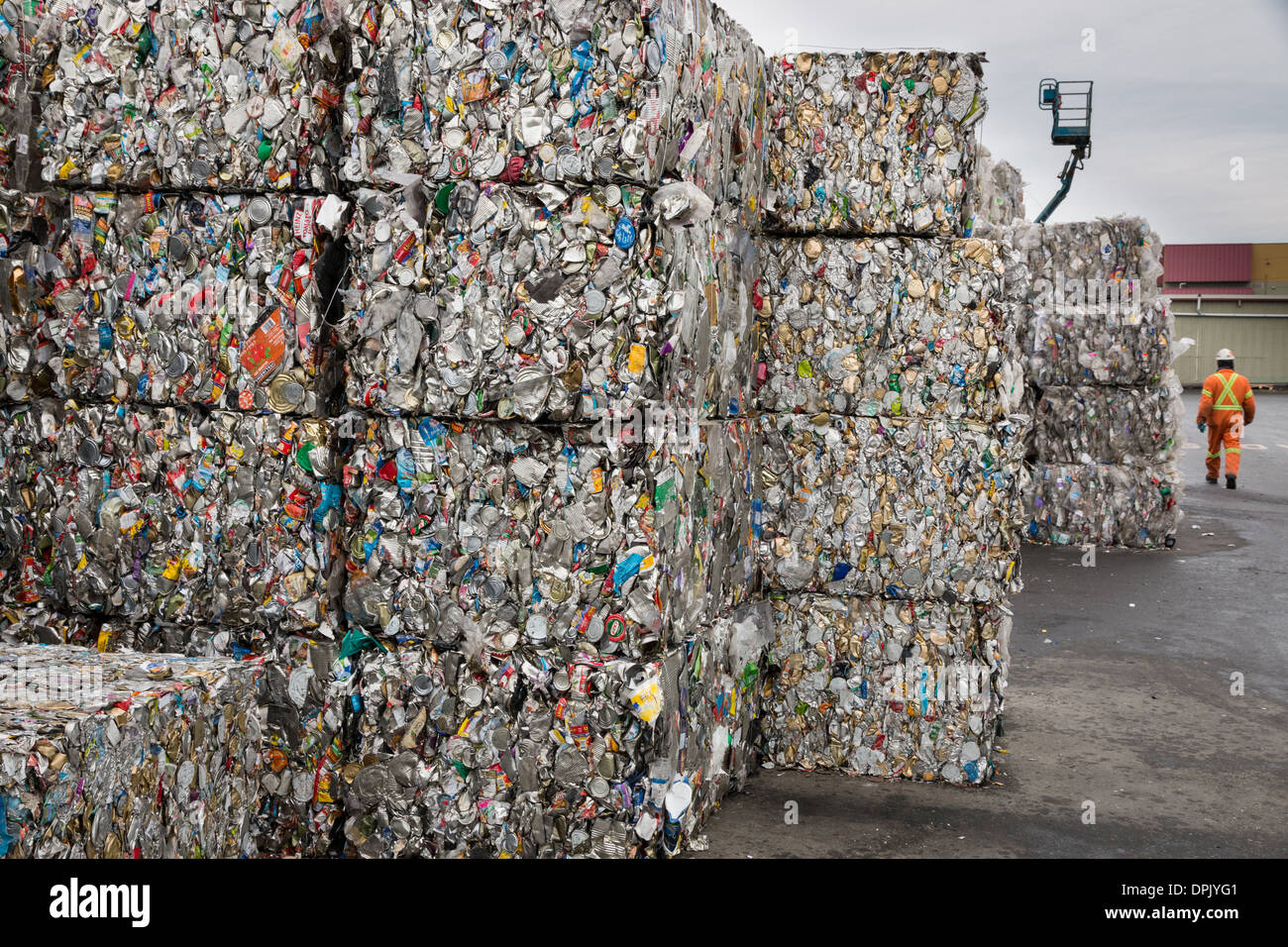 Ein Arbeiter geht vorbei an gestapelten Kuben aus aus zerkleinerten Metalldosen, die Versandkosten zu einer Recyclinganlage besitzen zu erwarten. Stockfoto