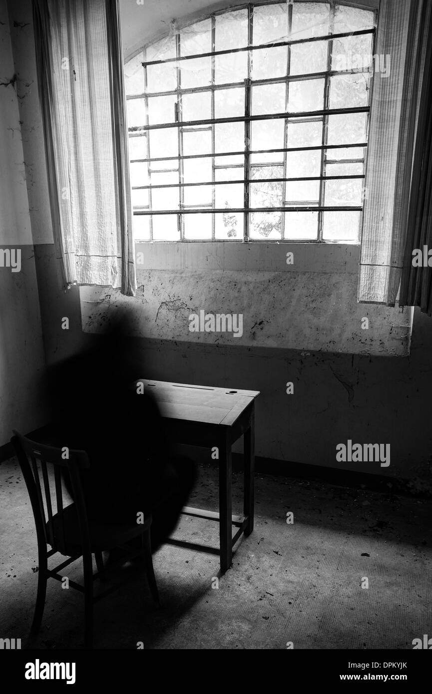 Einsame Person, die in trostlosen Zimmern mit Bars am Fenster sitzt Stockfoto