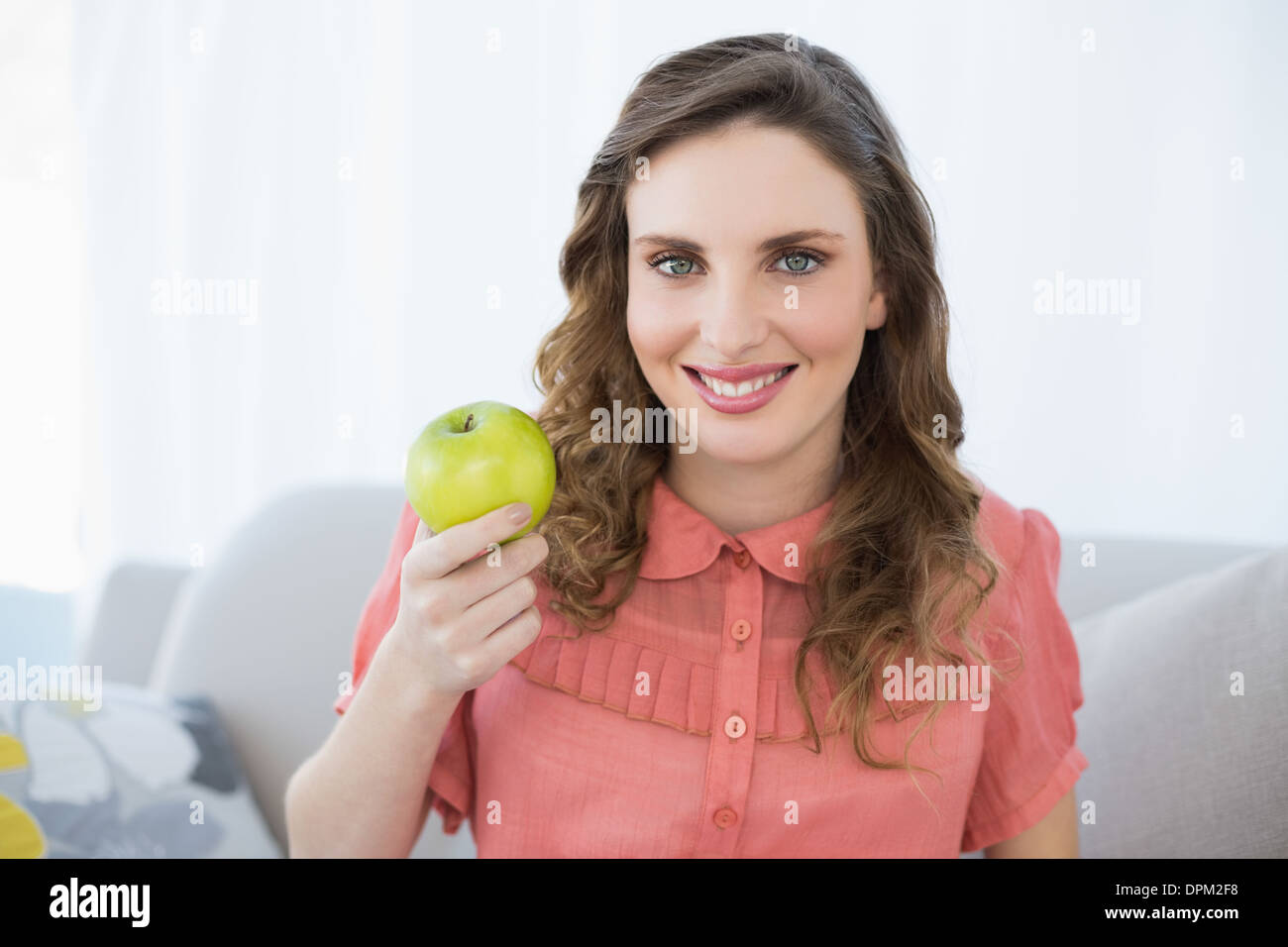 Schwangere Frau mit grünem Apfel im Wohnzimmer sitzen lächelnd Stockfoto
