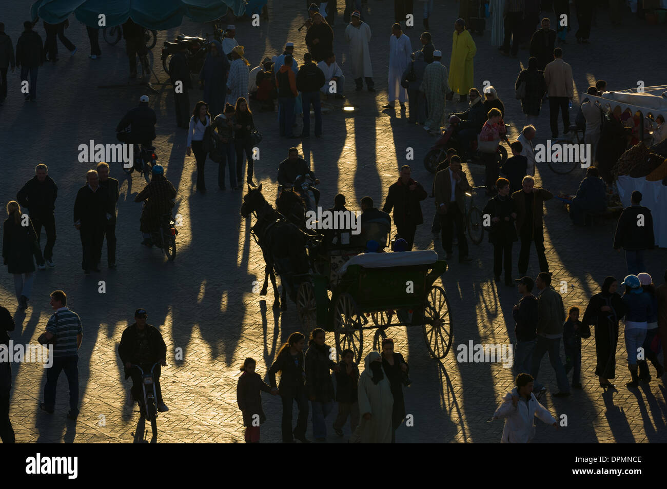 Fußgänger und eine Pferdekutsche werfen lange Schatten in der Djemaa el-Fna Platz bei Sonnenuntergang, Marrakesch, Marokko Stockfoto