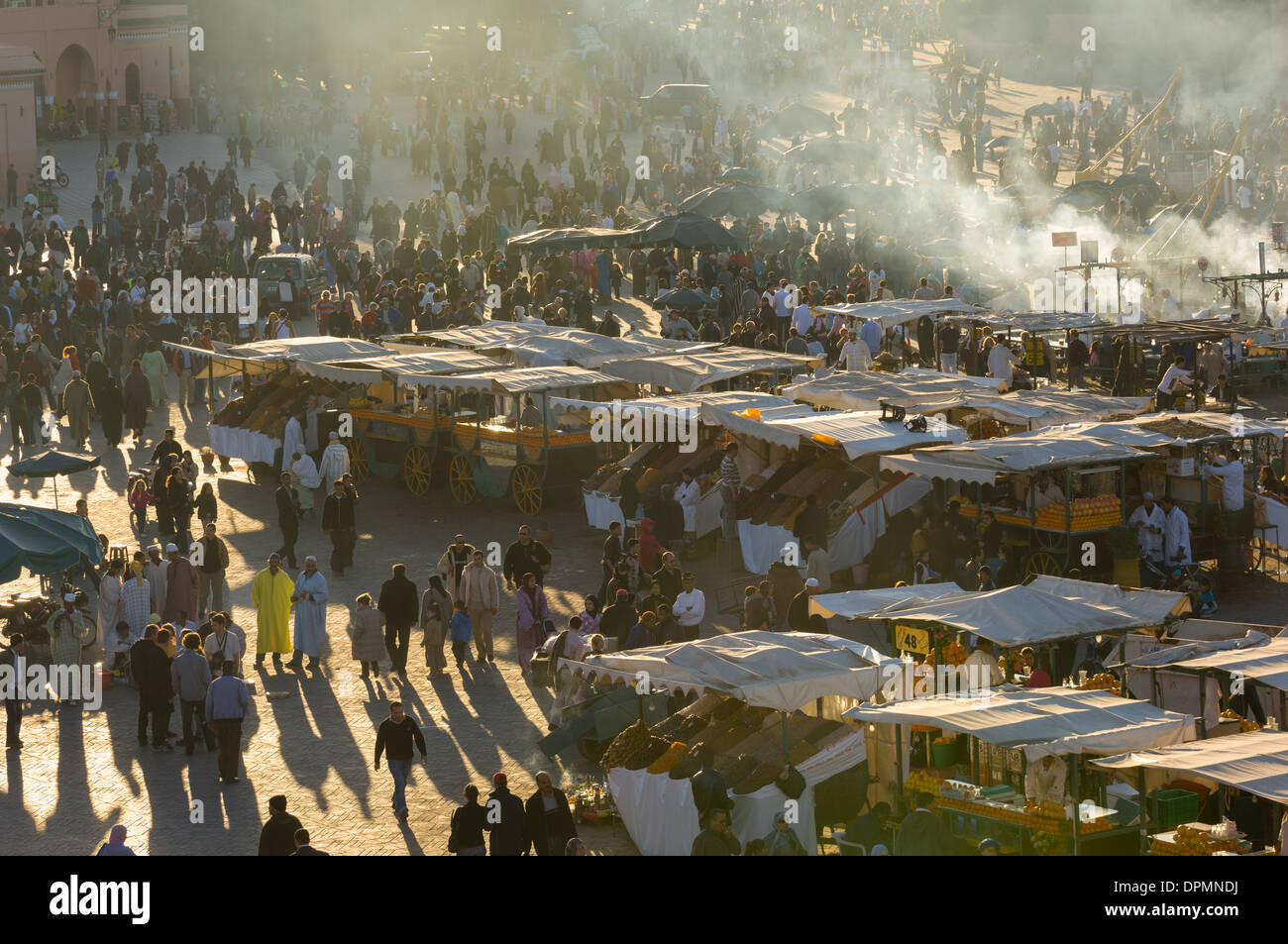 Passanten werfen lange Schatten inmitten Essen Stände verkaufen Termine und Trockenfrüchte in dem Djemaa el-Fna Platz bei Sonnenuntergang, Marrakesch, Marokko Stockfoto