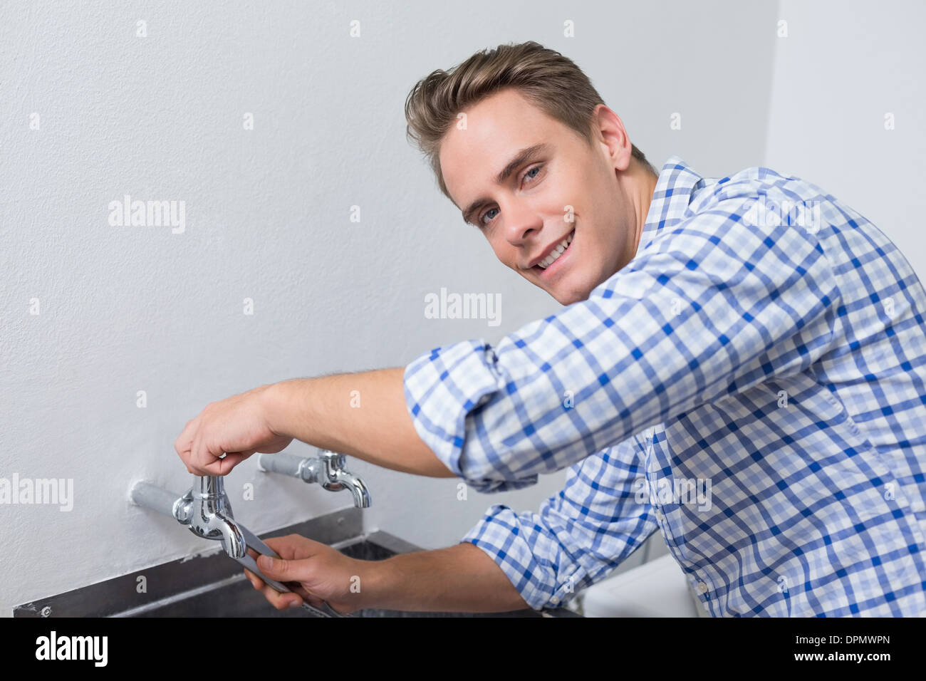 Lächelnde Klempner Wasserhahn mit einer Zange befestigen Stockfoto