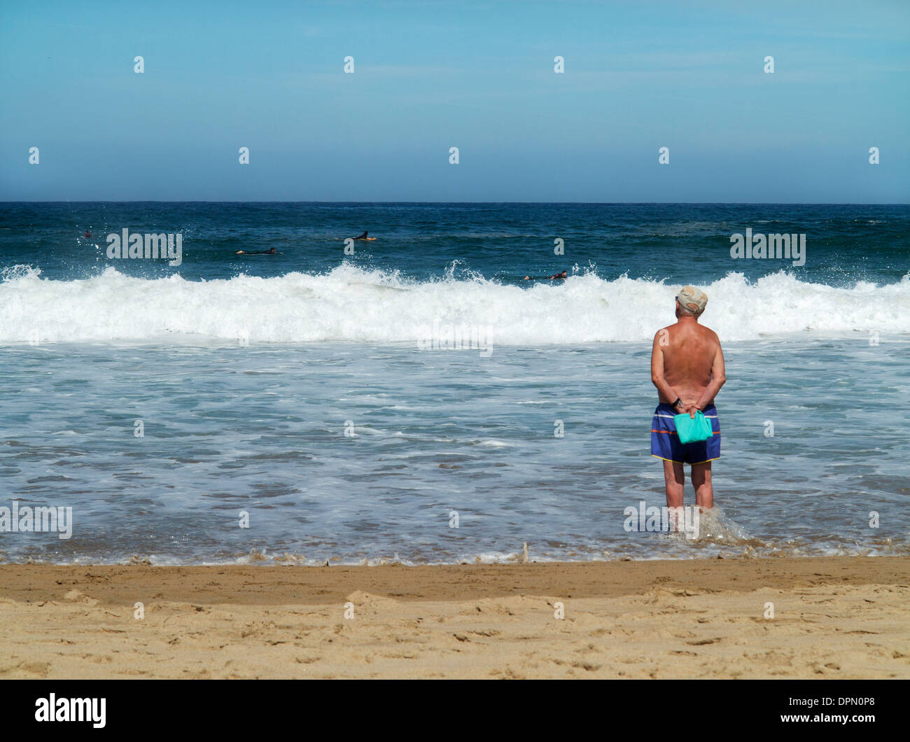 Ältere Mann in Badeshorts mit Blick aufs Meer auf La Zurriola Strand in San Sebastian, Spanien, wie Wellen am Ufer Stockfoto