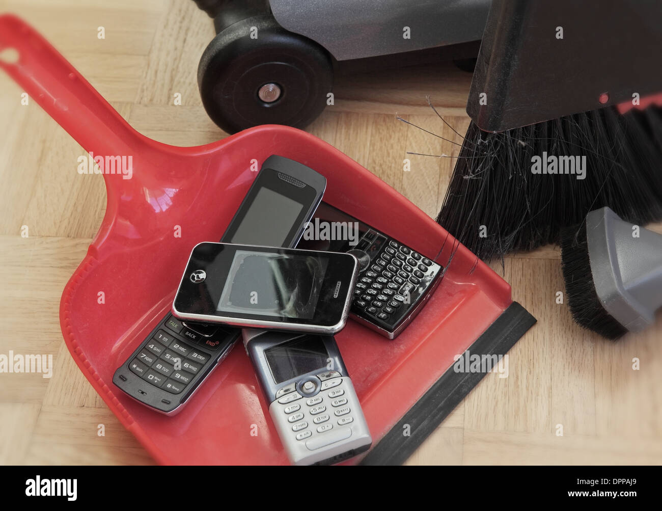 auf der Kehrschaufel sehen wir einige Handys bereit zur Wiederverwertung oder Schrott. Wir sehen auch ein paar Details von Besen und Staubsauger Stockfoto