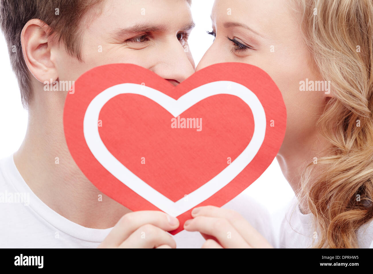Zwei junge Termine hinter Papierherz mit ihren Gesichtern nahe beieinander Stockfoto