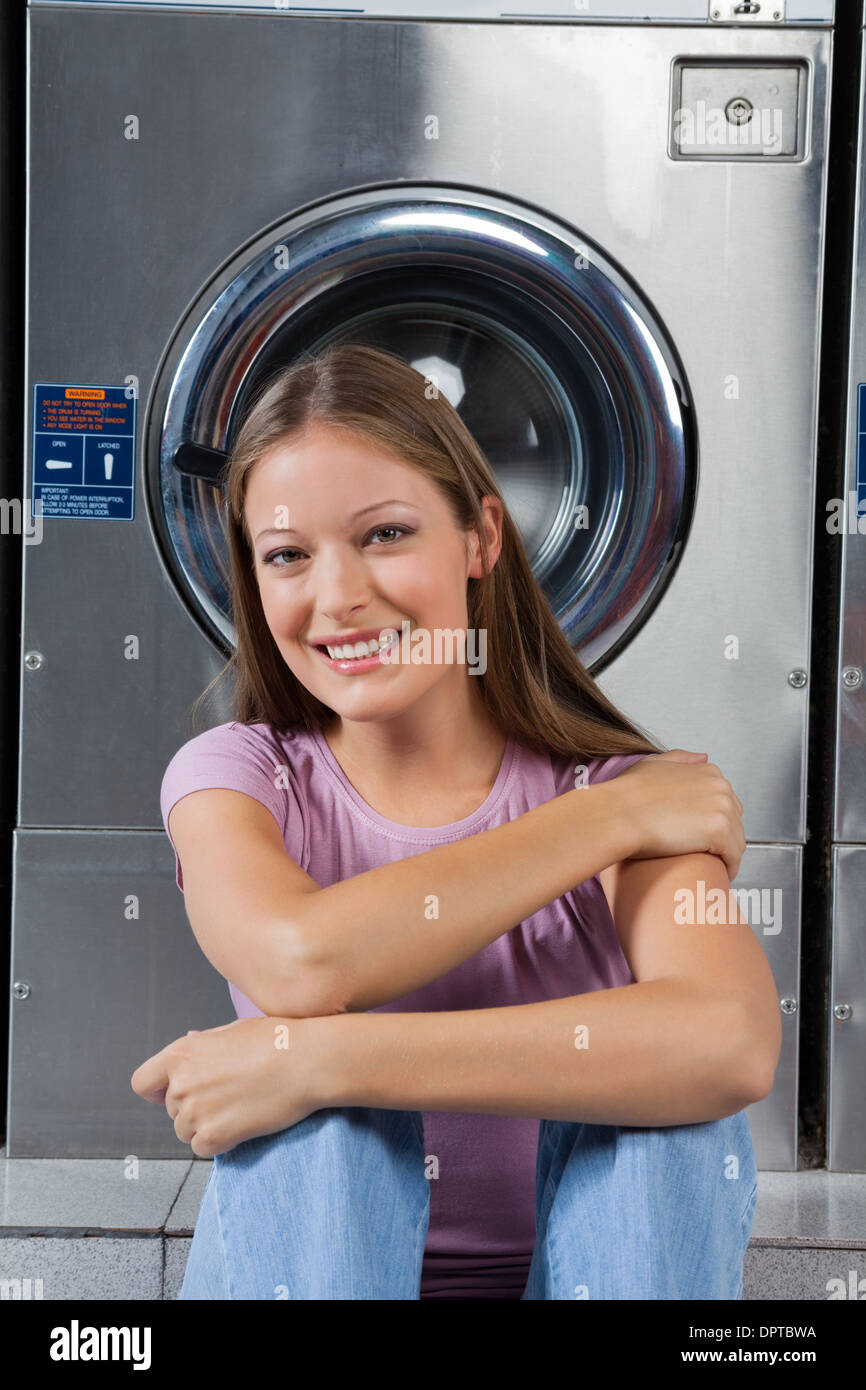 Schöne Frau sitzen gegen Waschmaschine Stockfoto