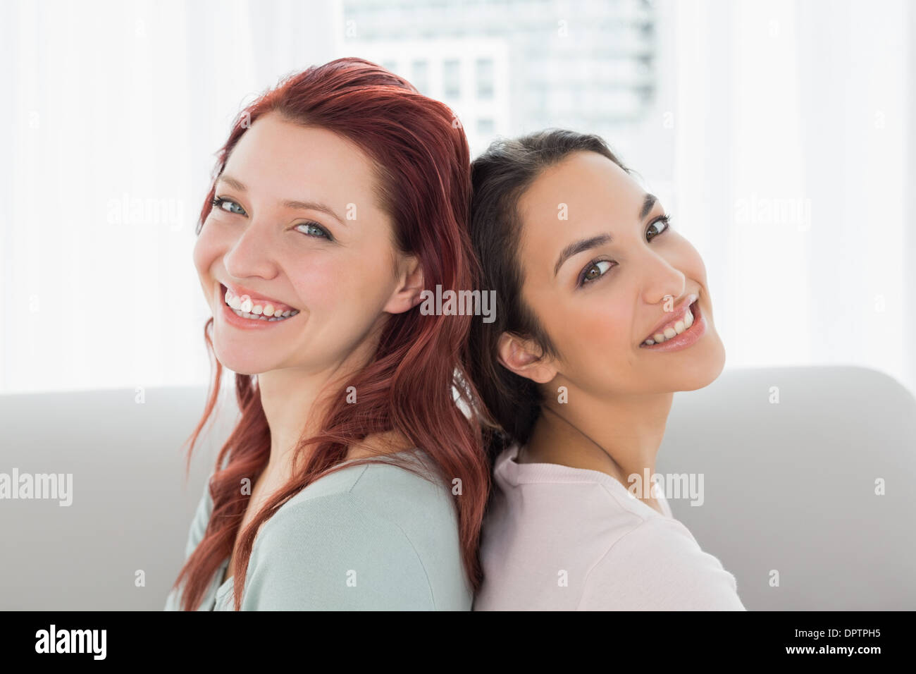 Schöne junge Freundinnen sitzen Rücken an Rücken zu Hause Stockfoto