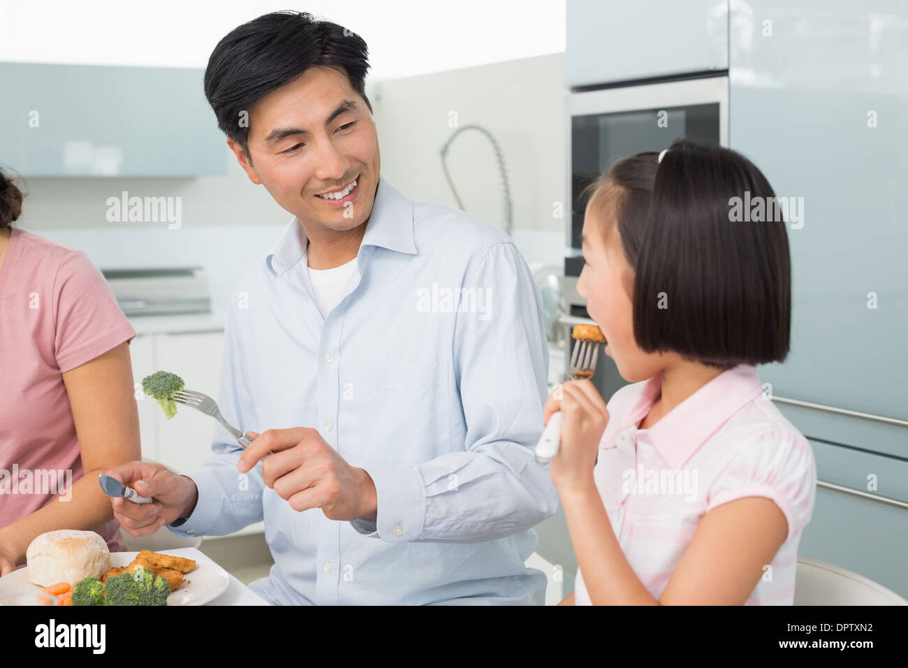 Vater beobachtete kleine Mädchen Essen mit einer Gabel in Küche Stockfoto