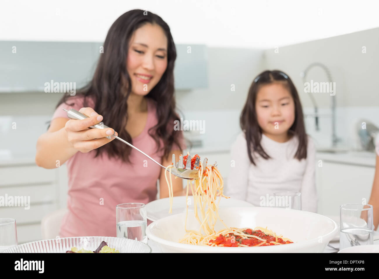 Kleine Mädchen beobachten glückliche Frau dienen Spaghetti in Küche Stockfoto